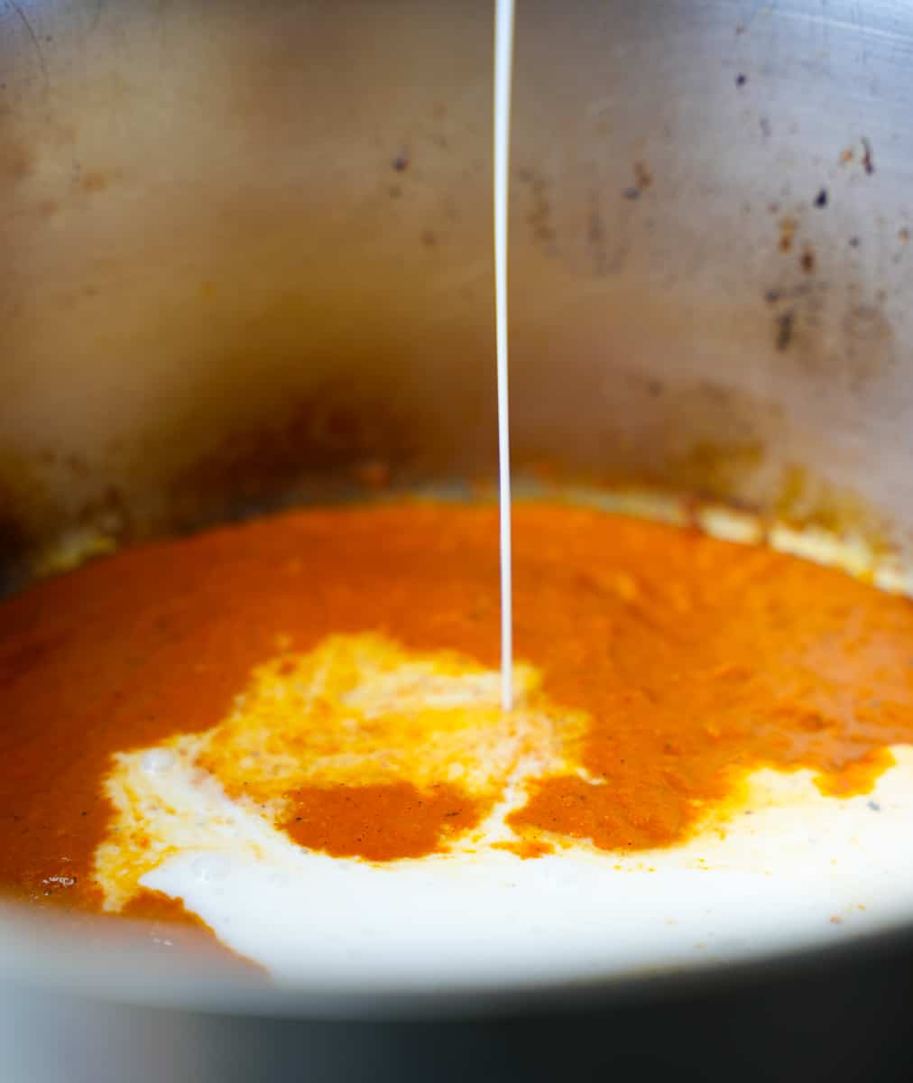 Coconut milk is pored into the sauce in a metal pot.
