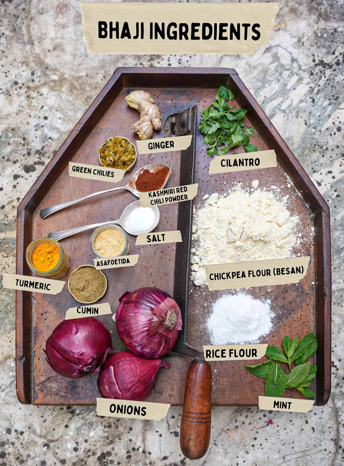 Bhaji ingredients are measured out and labeled on a wooden cutting board on top of a stone counter top.