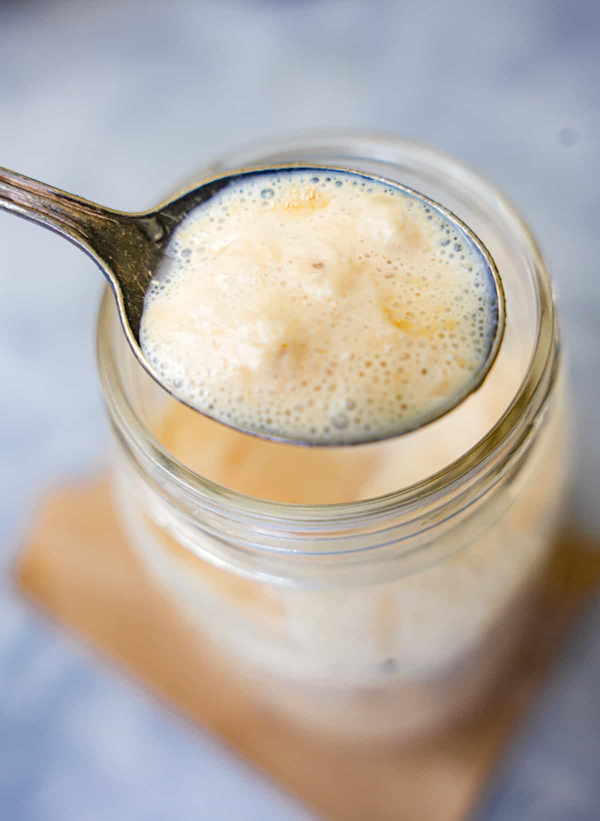 Bloomed yeast in a spoon above a jar.