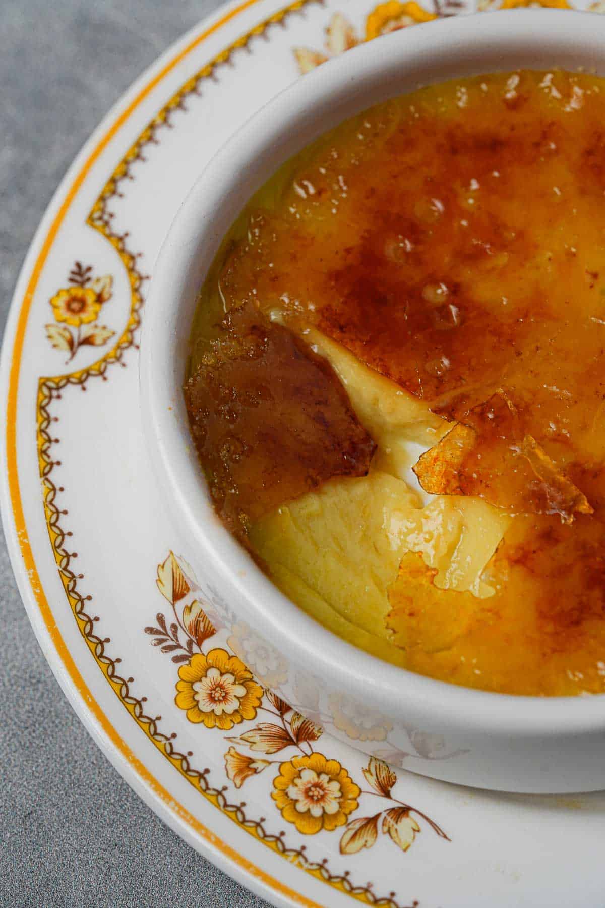 Close up of the cracked top of Vegan Creme Brulee in a white ramekin on a plate.