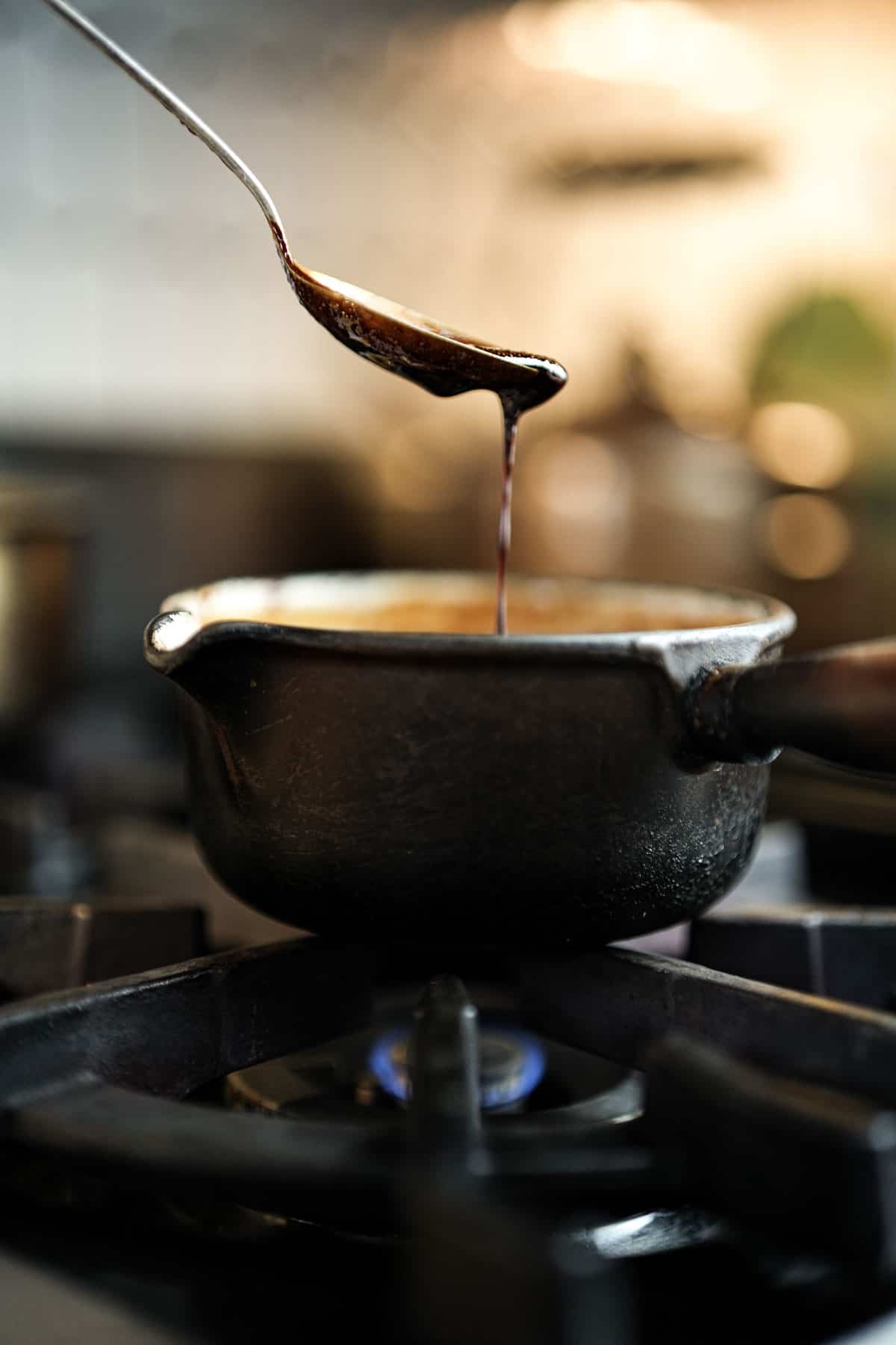 Kecap manis being simmered over a very low flame in a metal saucepan on the stove.
