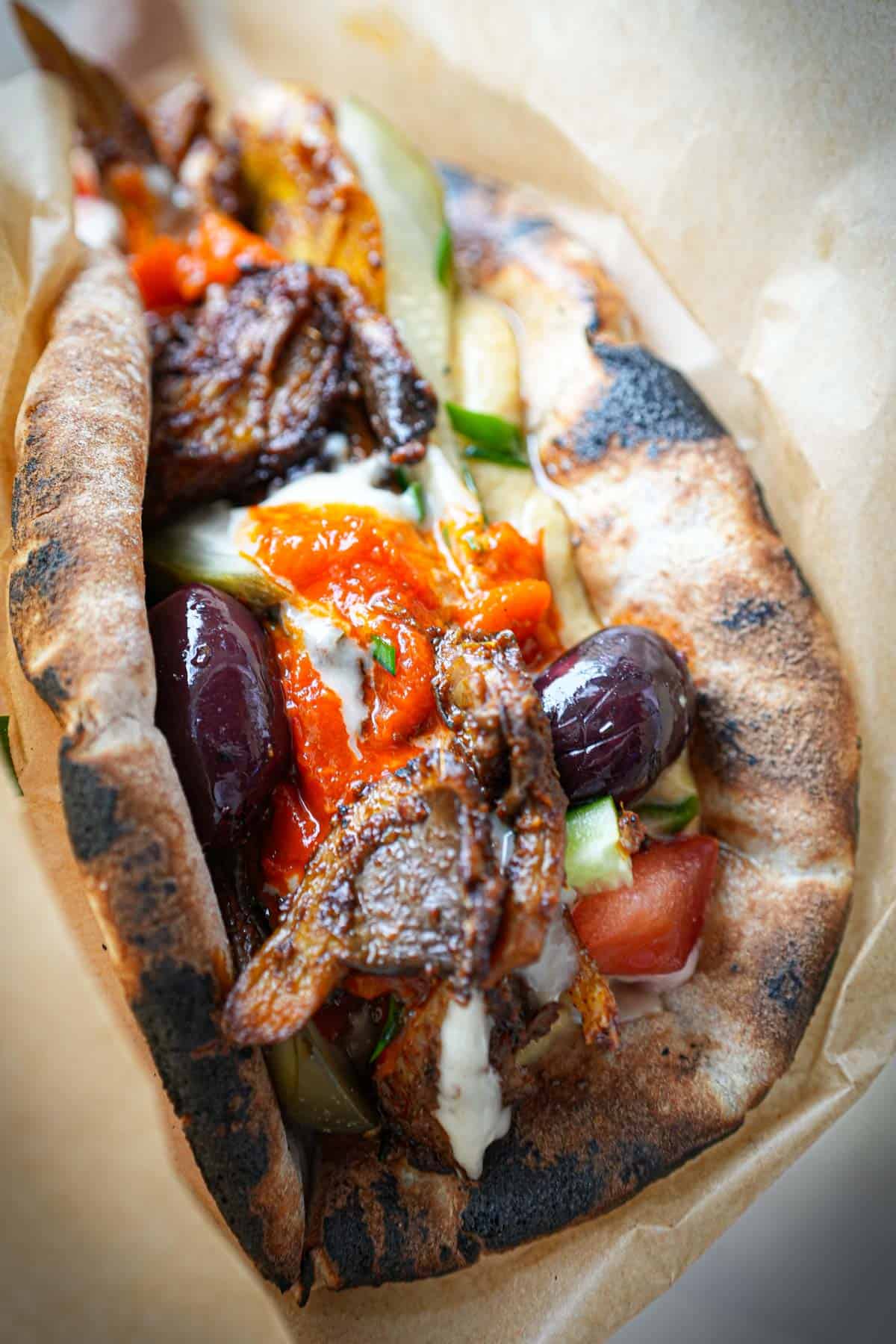 Vegan Shawarma Sandwich being held in brown craft paper. You can see the olives and sauce glistening in the light.