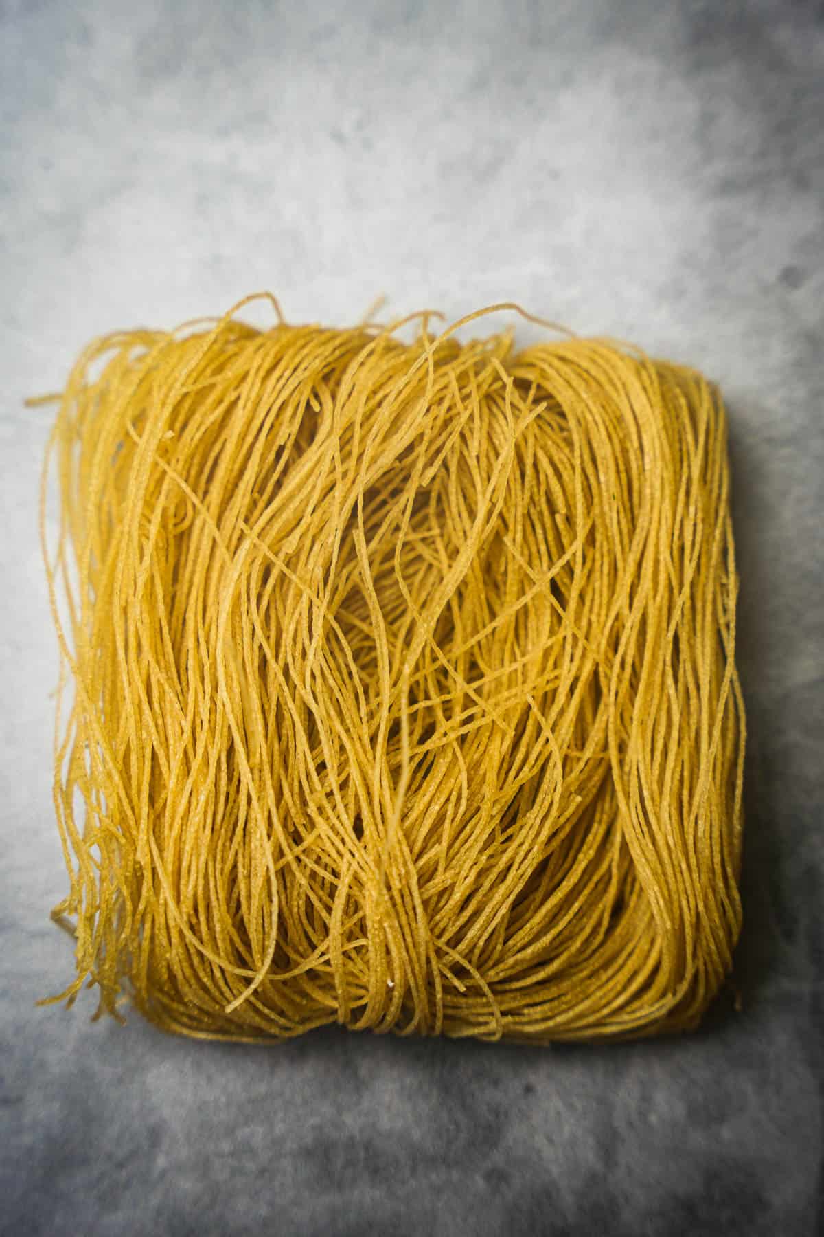 A square portion of dried gluten free vermicelli noodles.