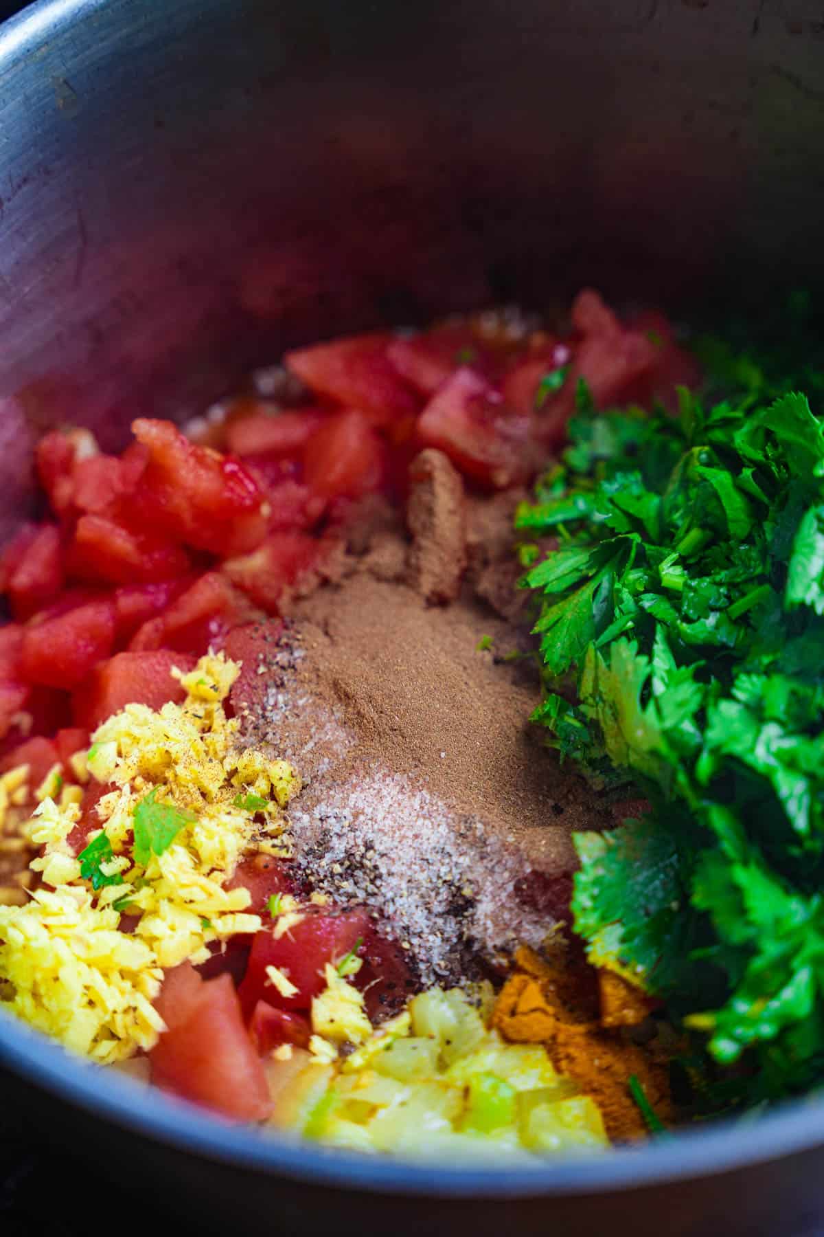 Diced tomatoes, parsley, cilantro, ginger, pepper, cinnamon, turmeric, and salt are added to the pot.