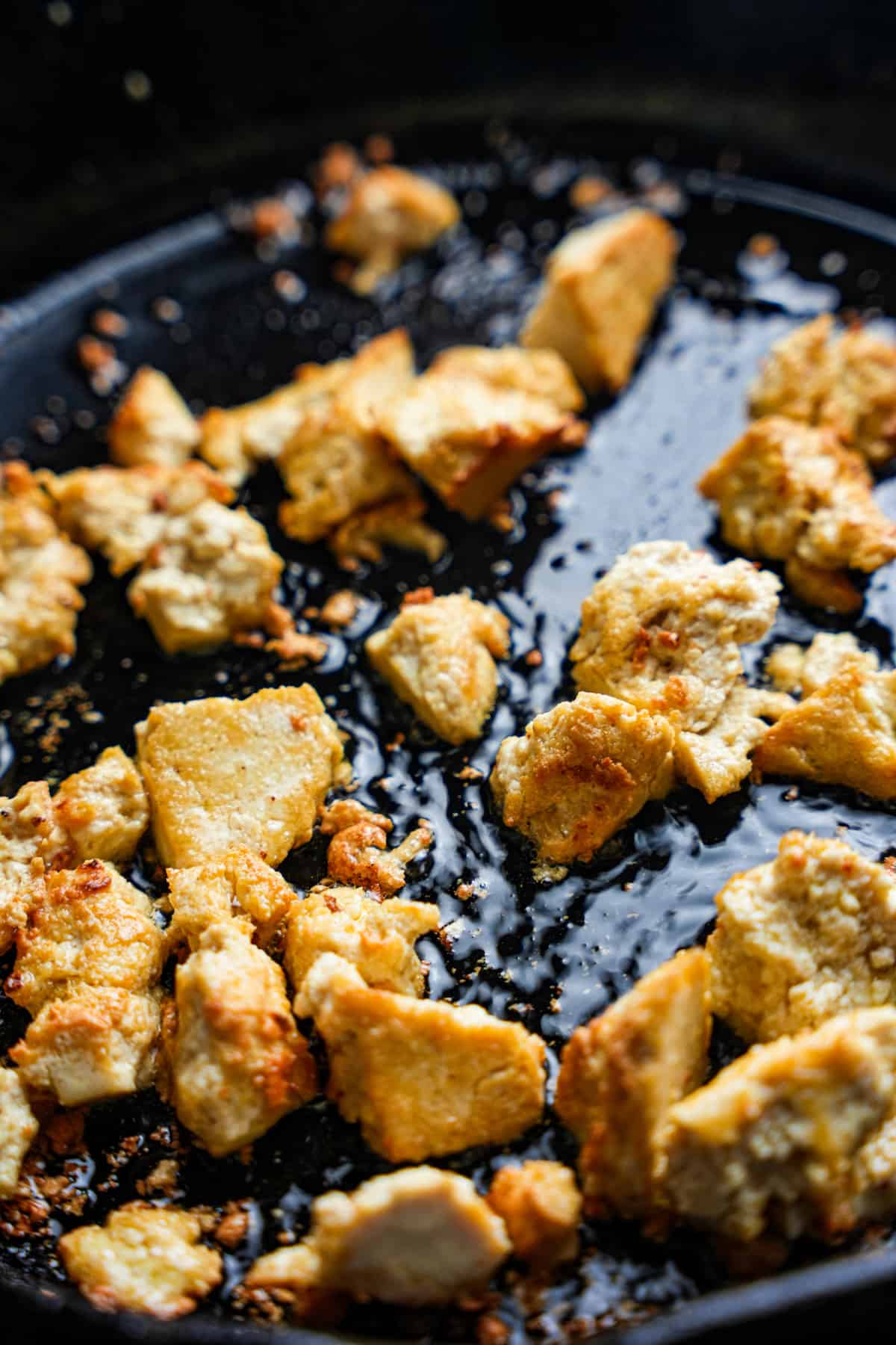 Torn pieces of tofu are pan-fried until golden brown in a cast iron skillet.