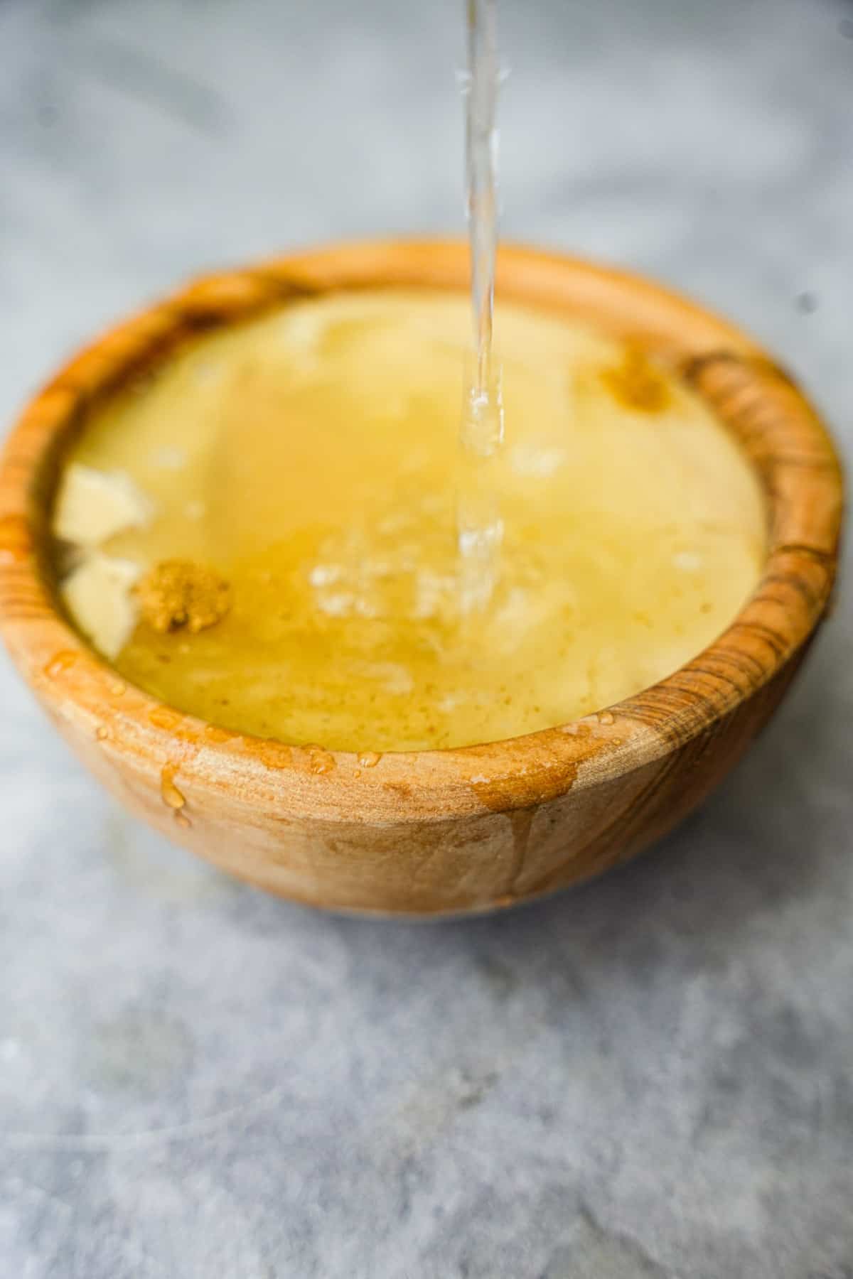 water is added to the tahini sauce ingredients in a wooden bowl.