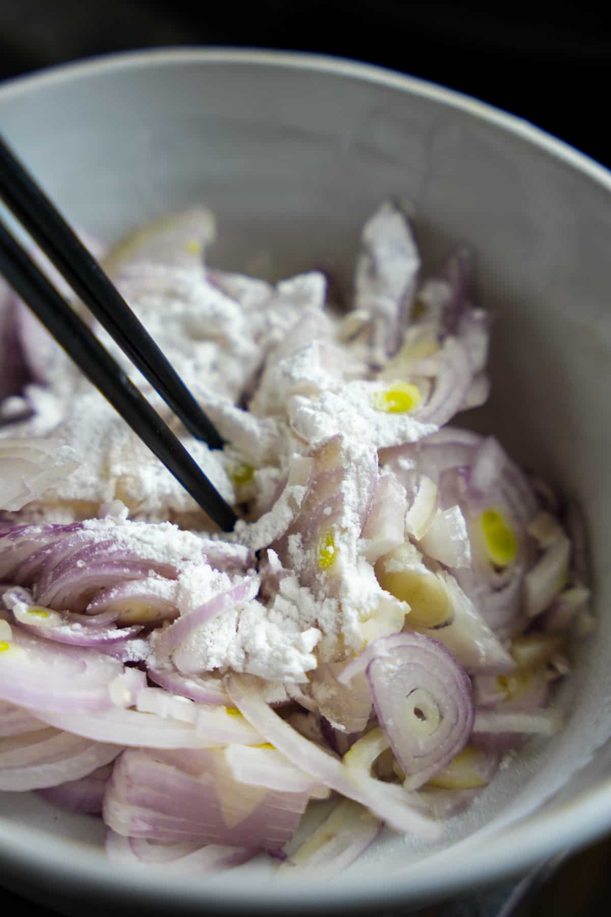 Mixing tapioca flour and sliced shallots with chop sticks in a bowl.