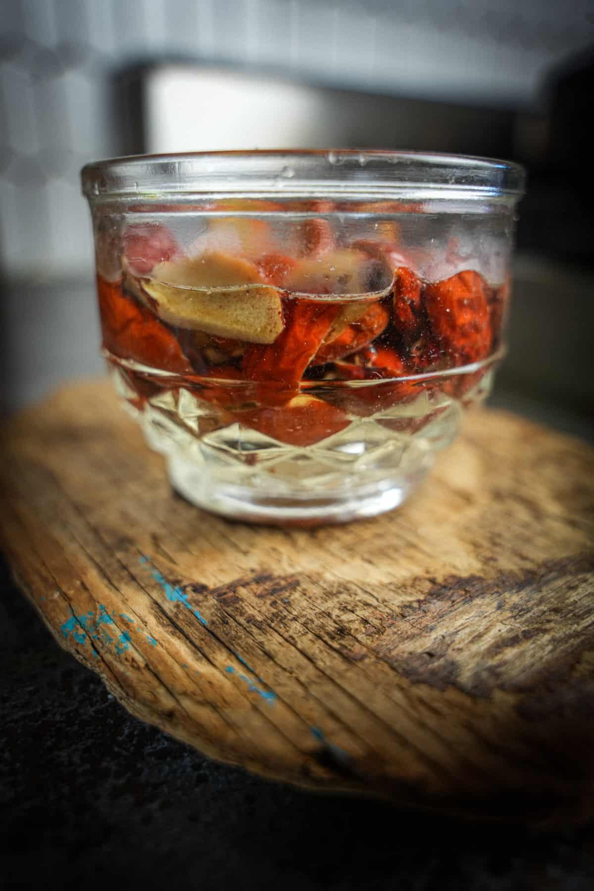 Red jujube dates soaking in a glass over a piece of wood.