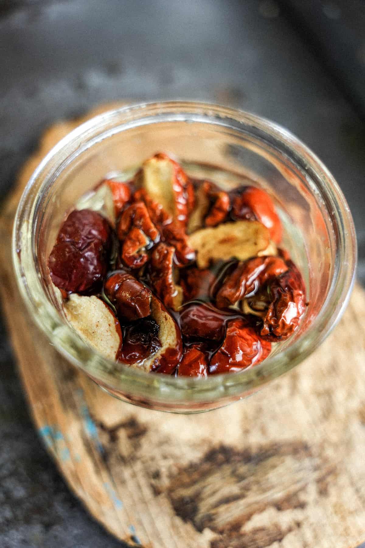 Red jujube dates soaking in a glass over a piece of wood.