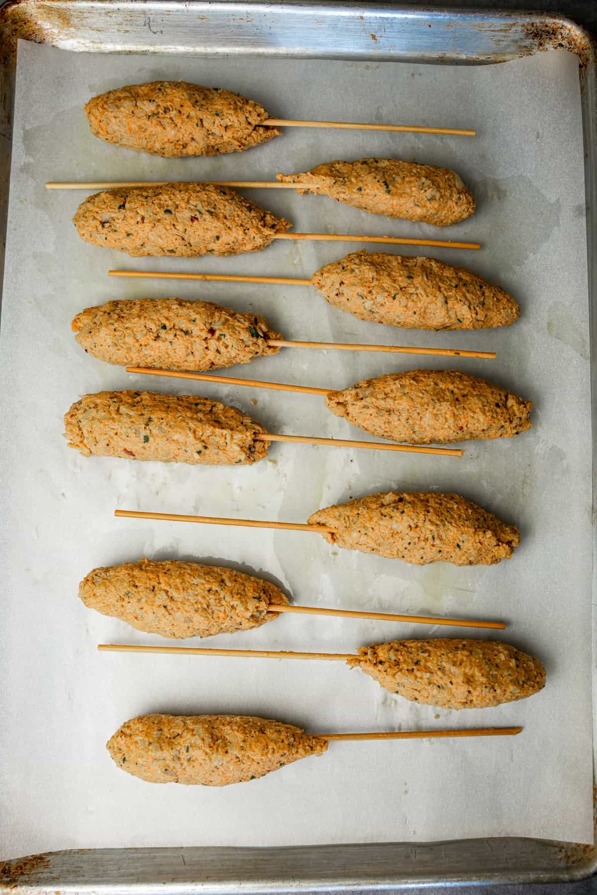 vegan kofta is formed and skewered on a parchment paper-lined baking pan.