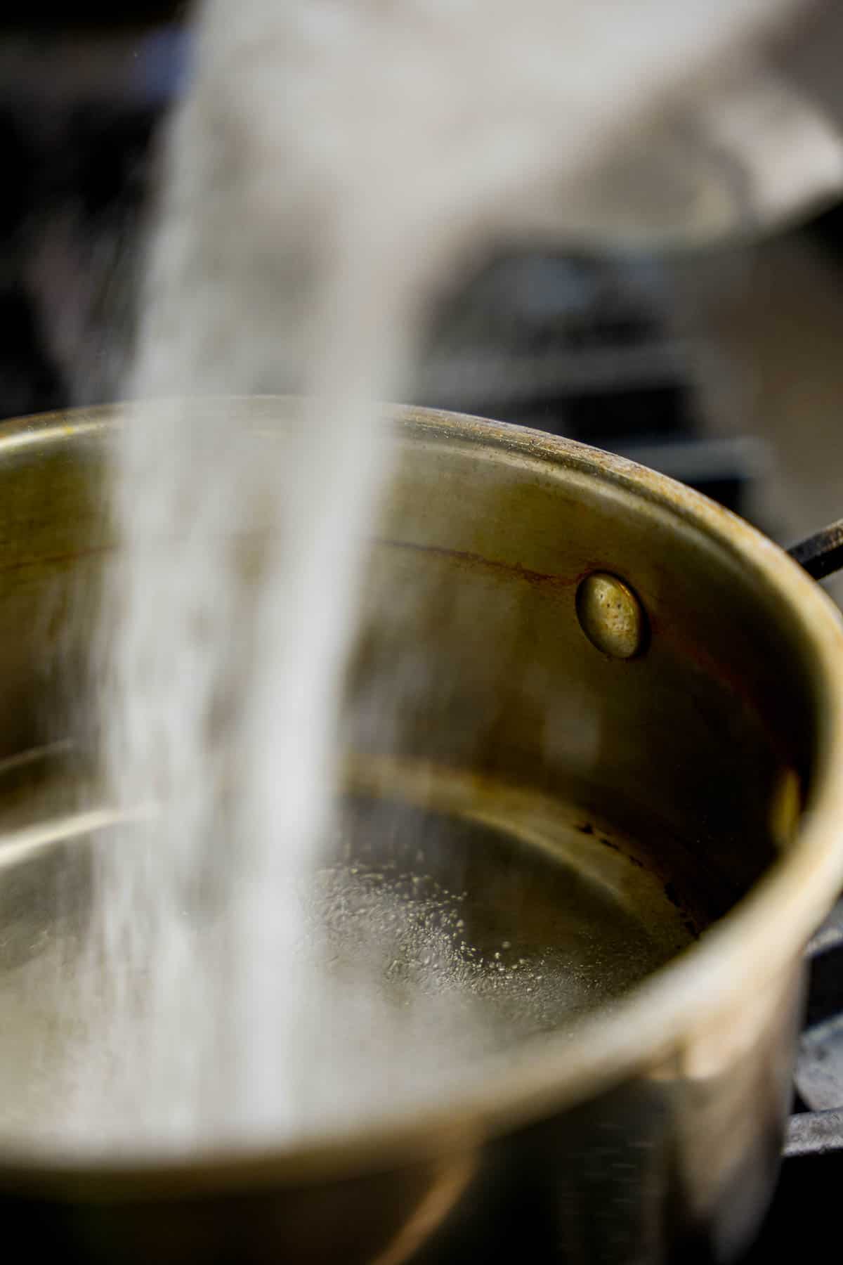 Sugar is poured into water in a saucepan to make sugar syrup for the halvah.