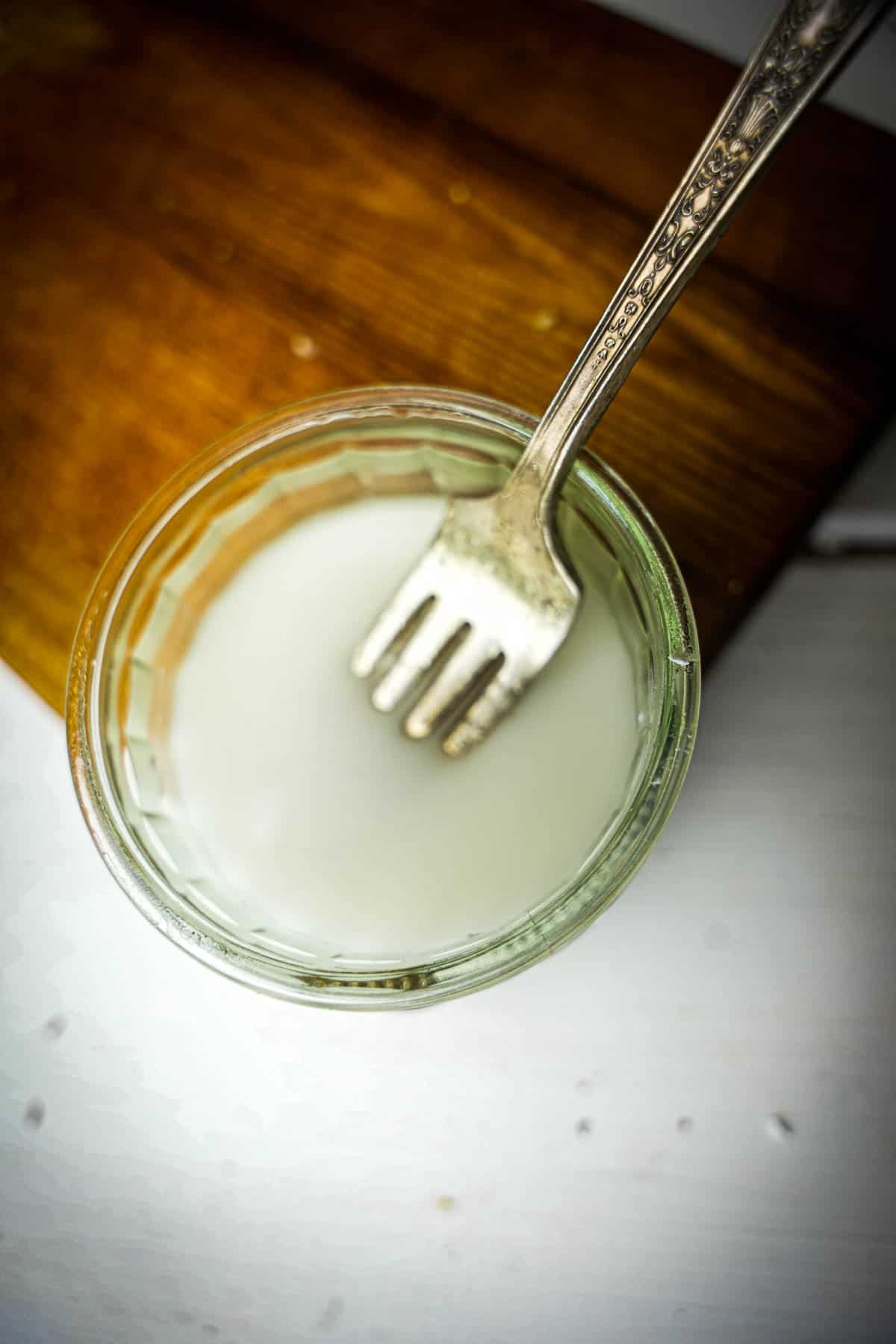Cornstarch and water are mixed together using a fork in a small glass.