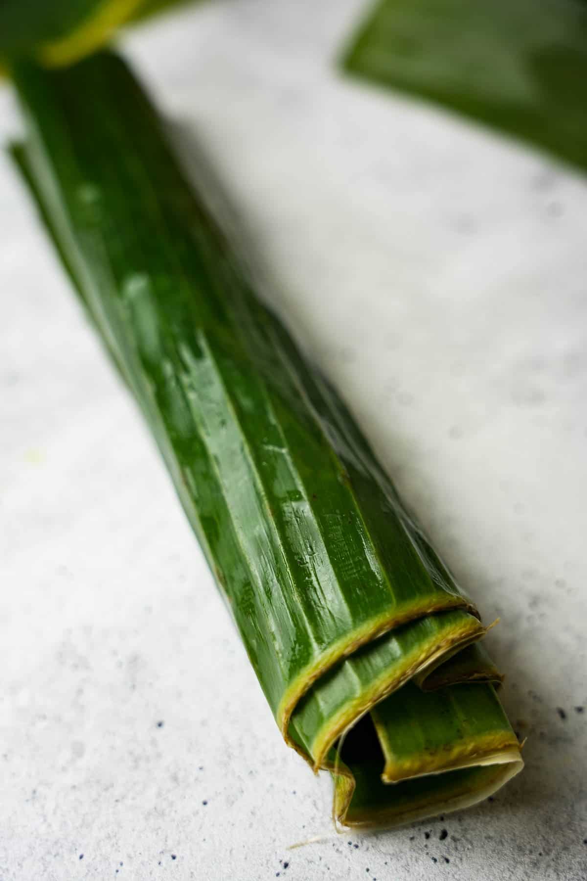 the filled banana leaf is rolled up into a long cylinder with open ends.
