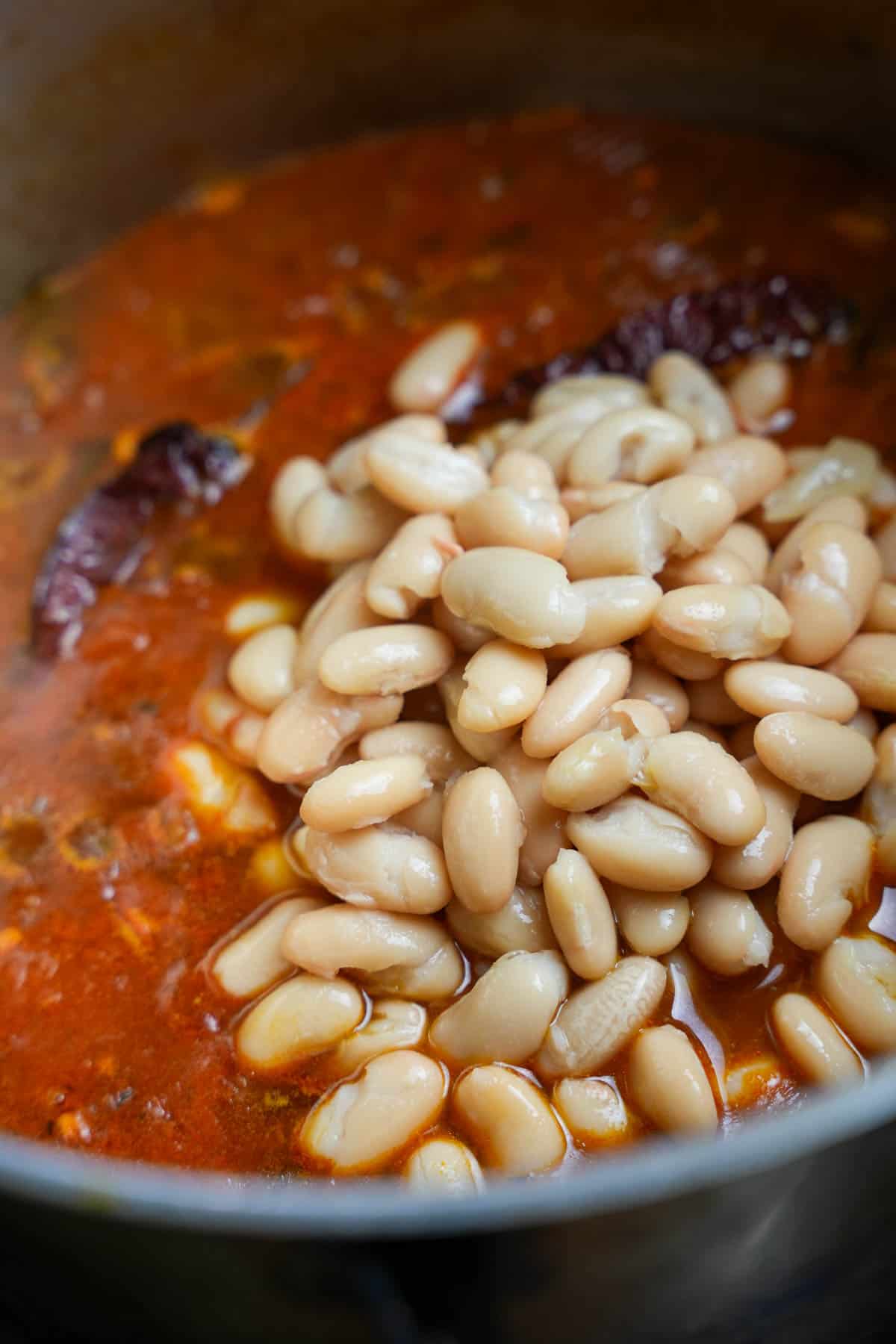 Once the stew is cooked and thick, cooked white beans are stirred into the stew base in the pot.