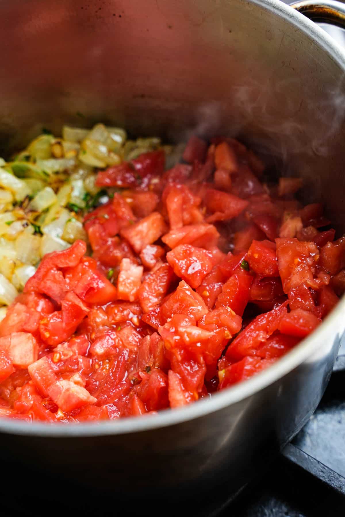diced tomatoes are added to the cooking onions, garlic, and parsley in a stainless steel pot.