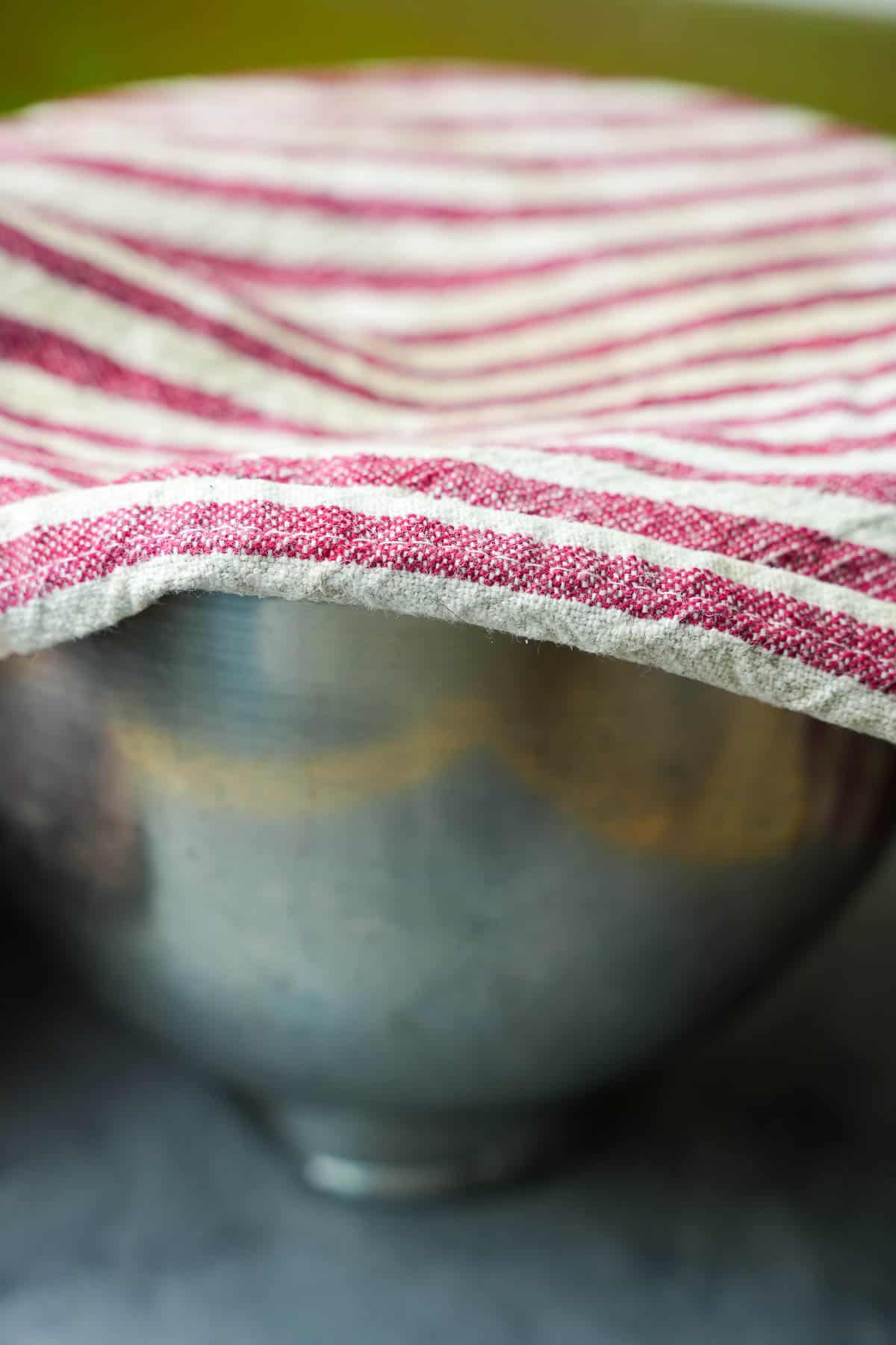 A bowl with dough is covered with a clean, slightly moistened kitchen cloth.