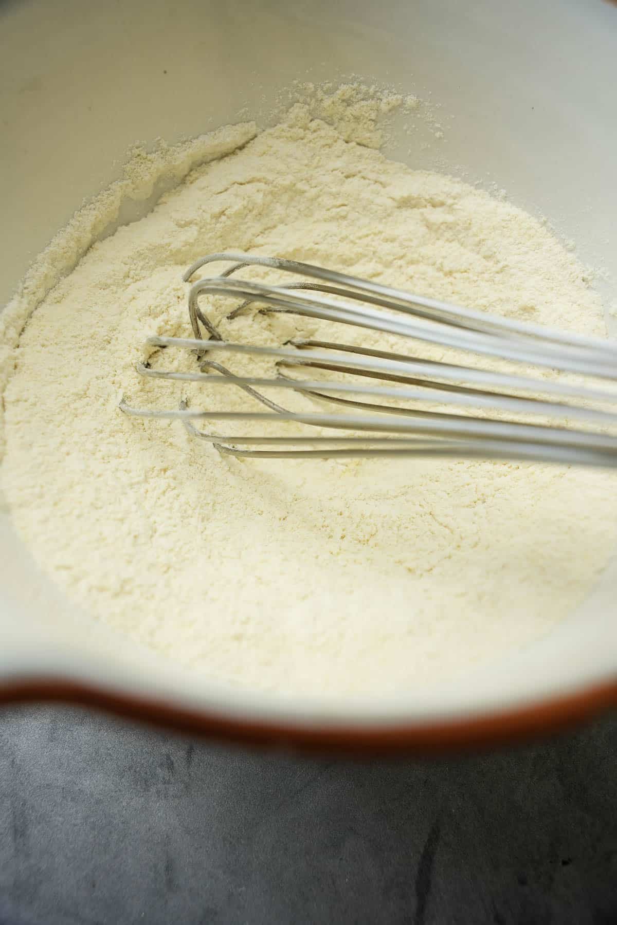 The dry ingredients are whisked together in a white ceramic mixing bowl.
