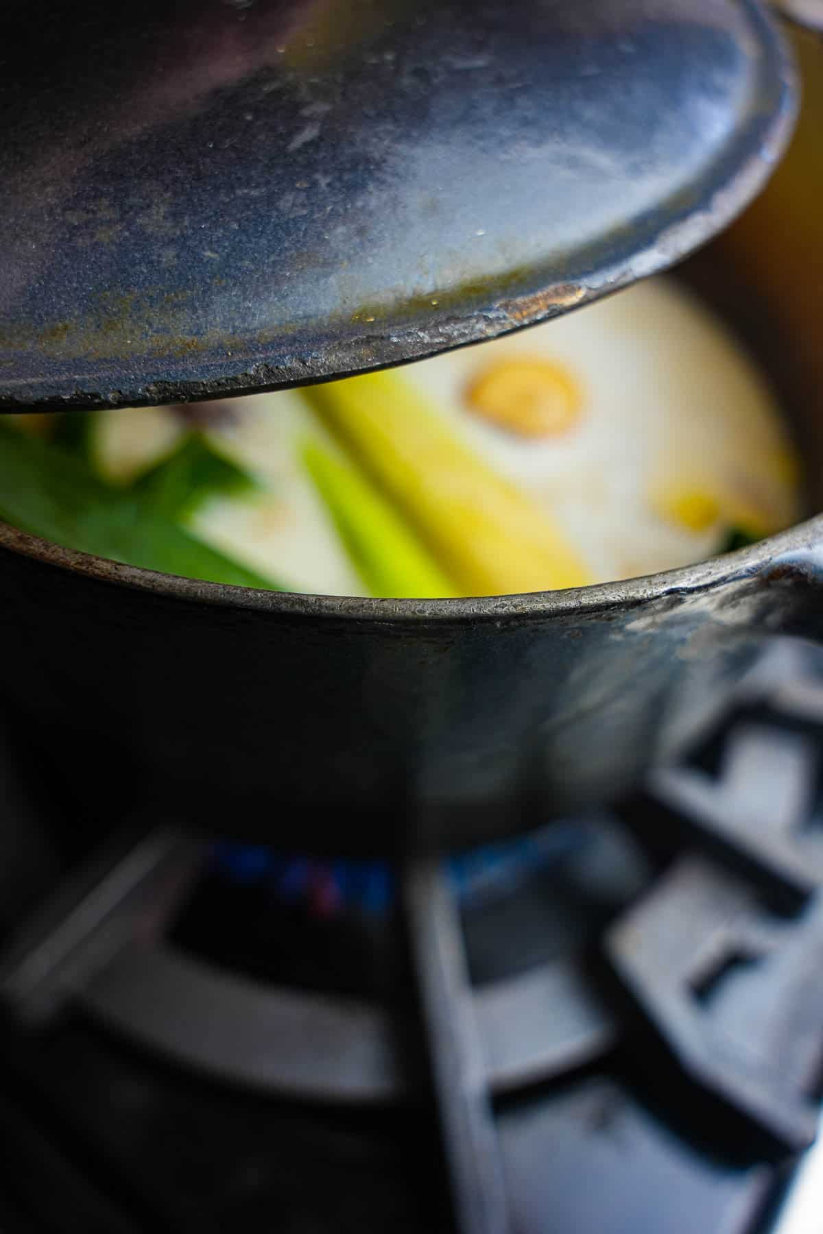 A lid is placed onto the cooking ingredients in a blue colored pot on the stove.