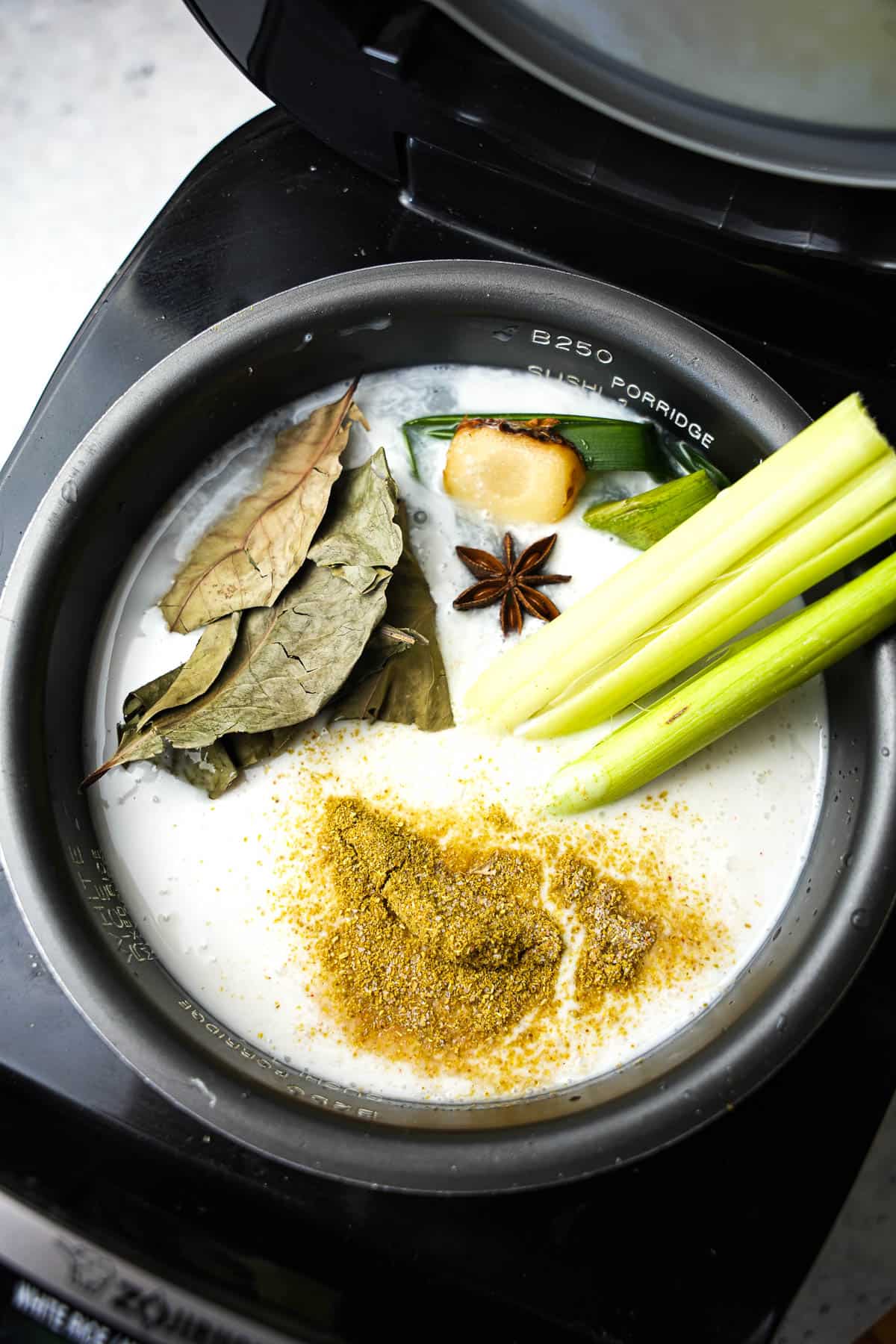 Rice is cooked in a rice cooker. You can see the Indonesian bay leaves, ginger, galangal, pandan, lemongrass, and star anise floating in the coconut milk.
