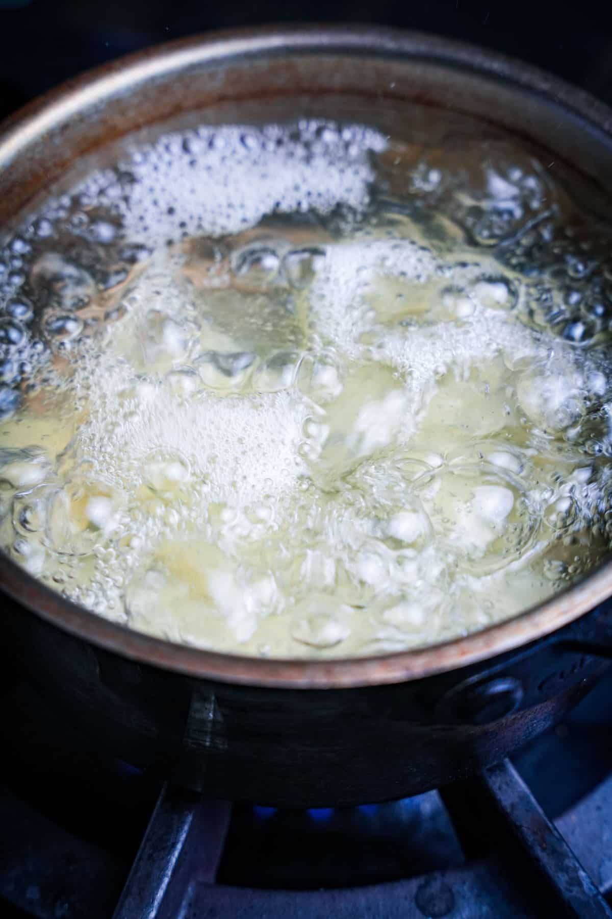 Potatoes boiling in a saucepan over a high flame.