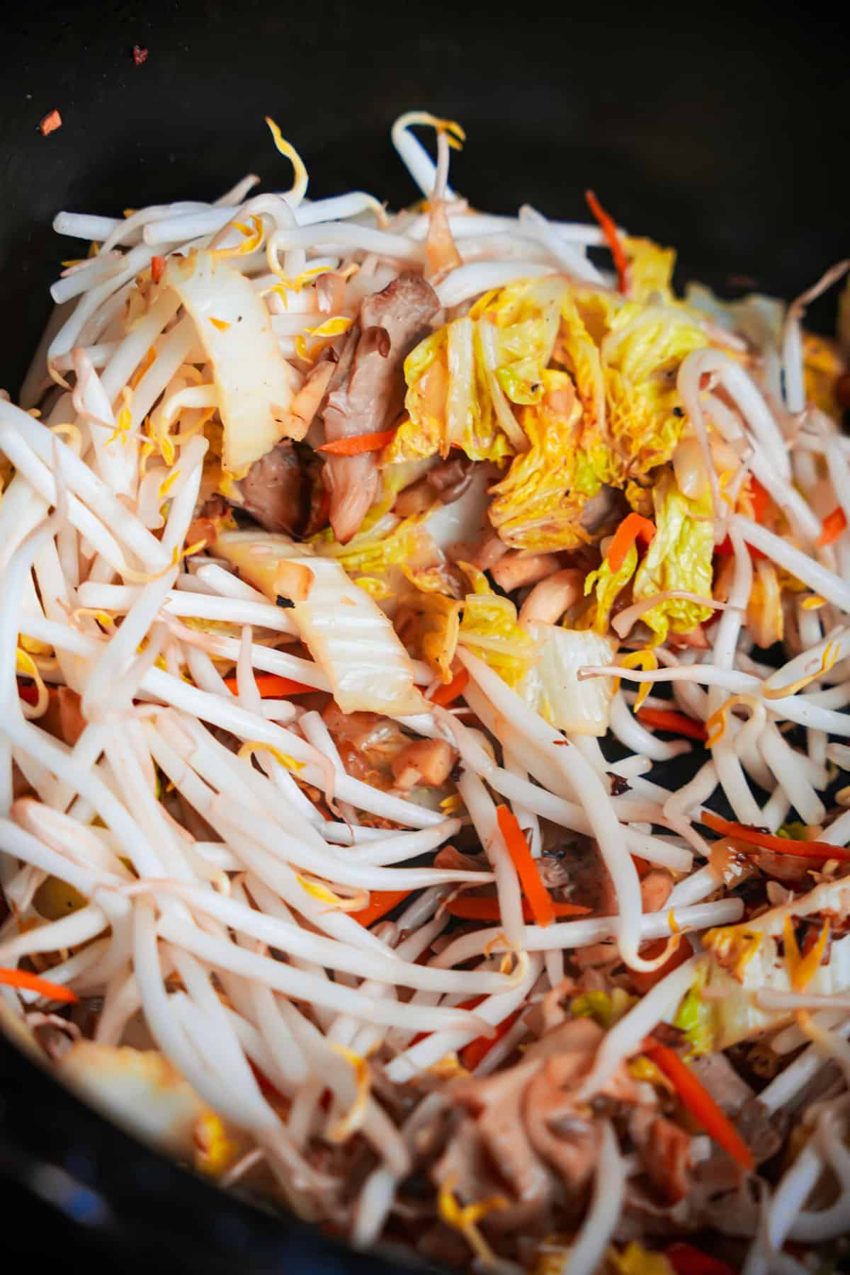 Bean sprouts are stirred into the stir-frying veggies in the pan.