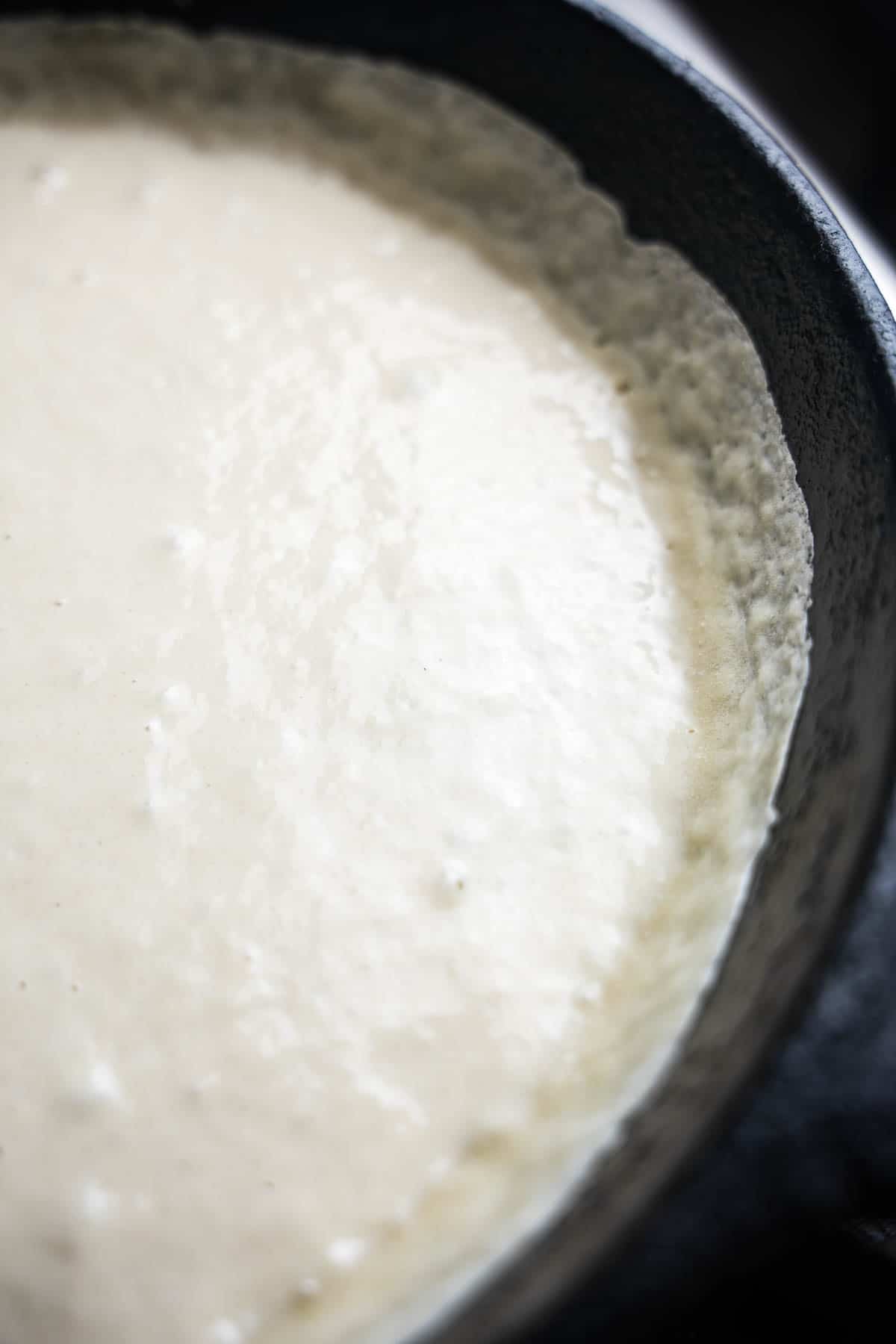 Batter is going up the sides of the pan forming a thin crisp edge all around the pancake.
