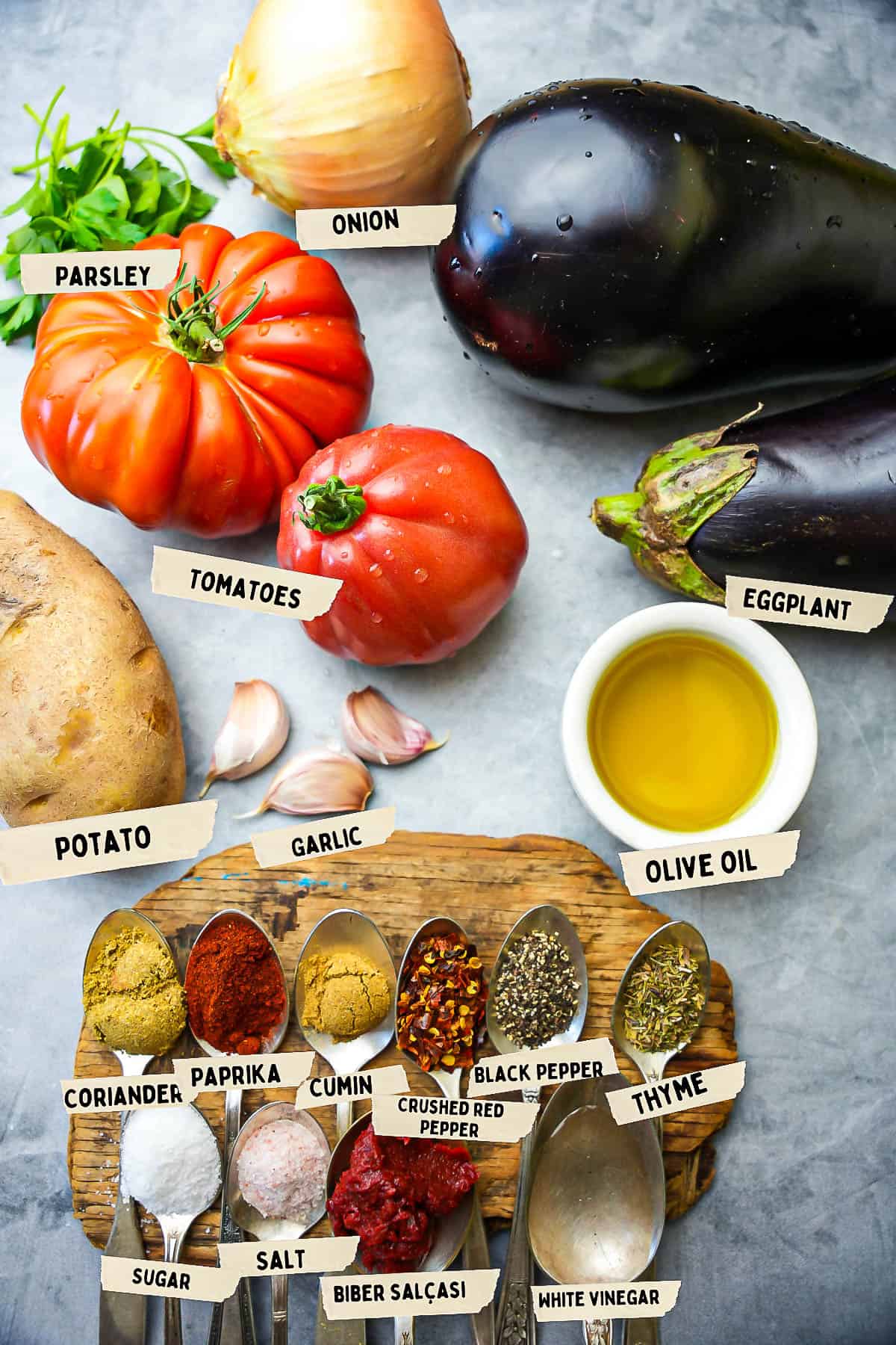 şakşuka ingredients laid out and labeled on a stone counter. All of the spices are in silver spoons on a wooden board.