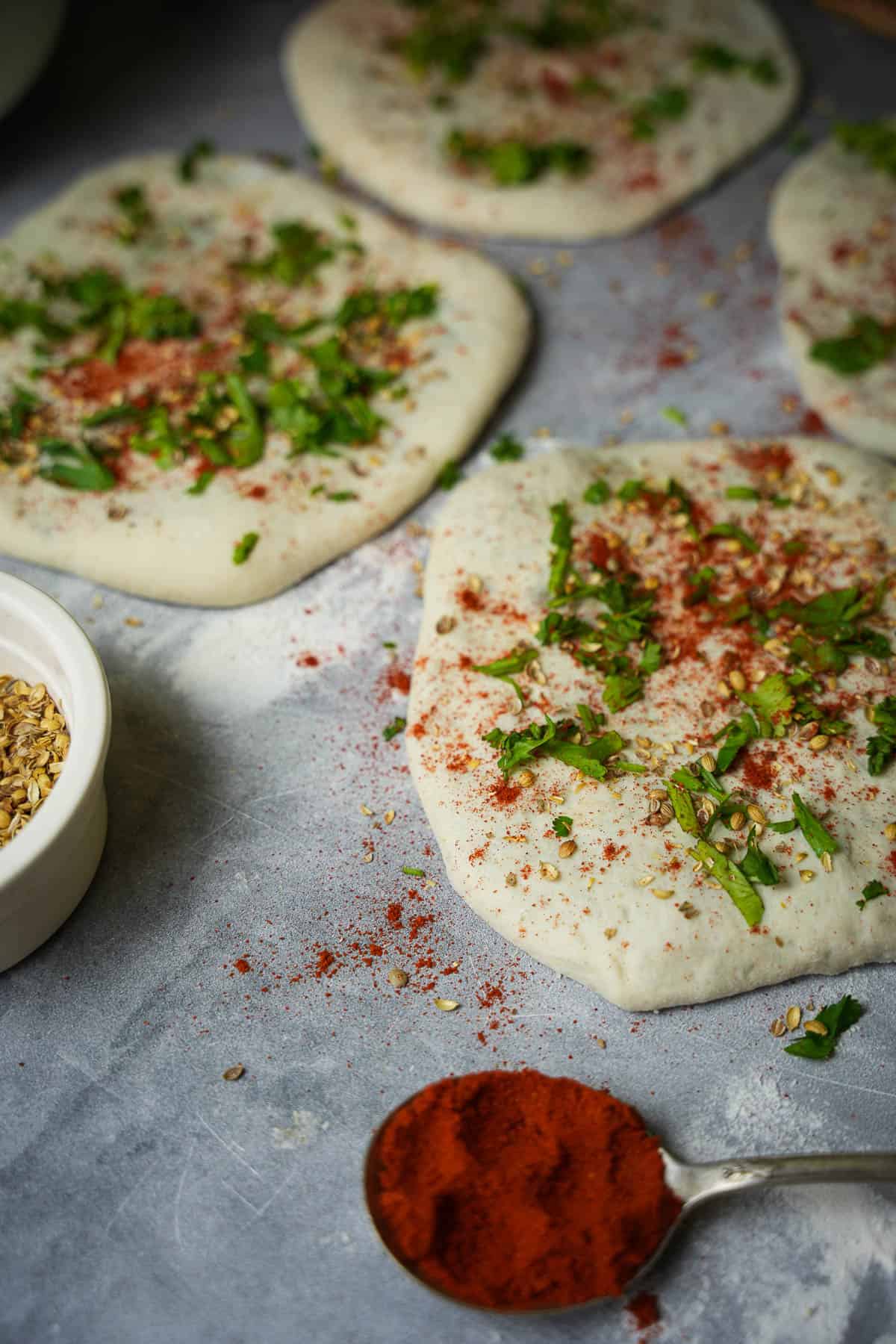 Formed kulcha are sprinkled with coriander seeds, kashmiri red chili and cilantro before being baked.