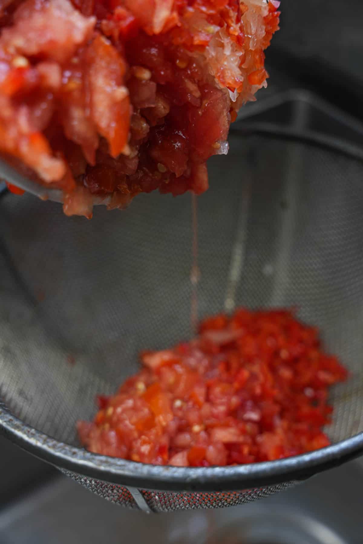 The minced tomatoes, onions and peppers are drained in a wire mesh strainer.