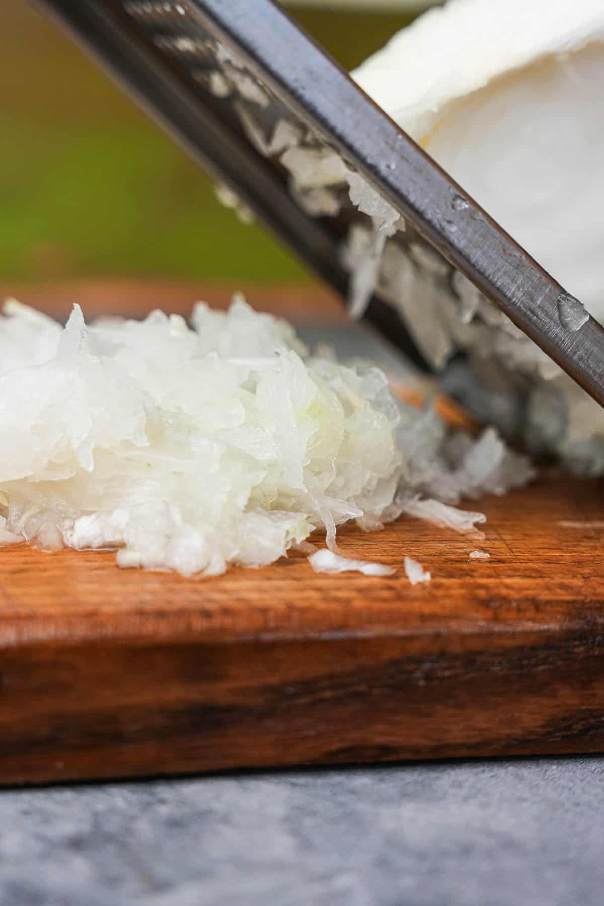 Onions being shredded by hand onto a wooden board.