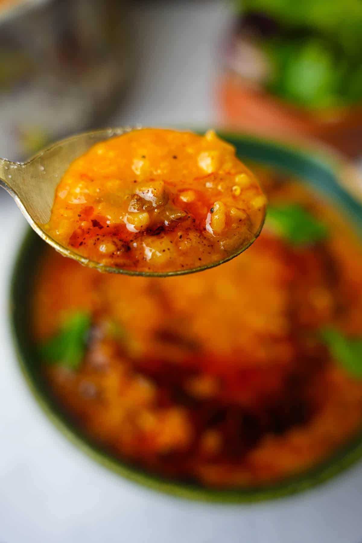 A spoonful of ezogelin held up above a bowl of the soup.
