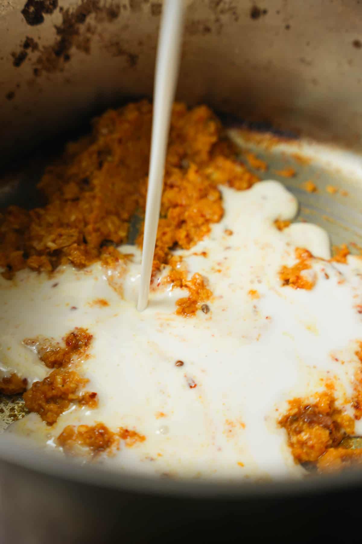 Coconut milk is added to the fried curry paste in a stainless steel pot.