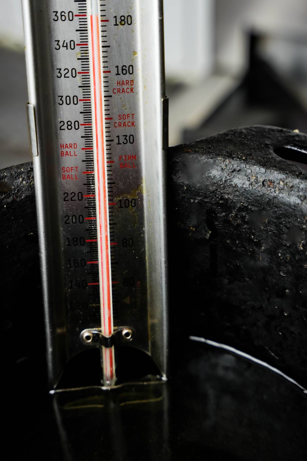 The temperature of oil being heated in a pot is tested using a candy thermometer.