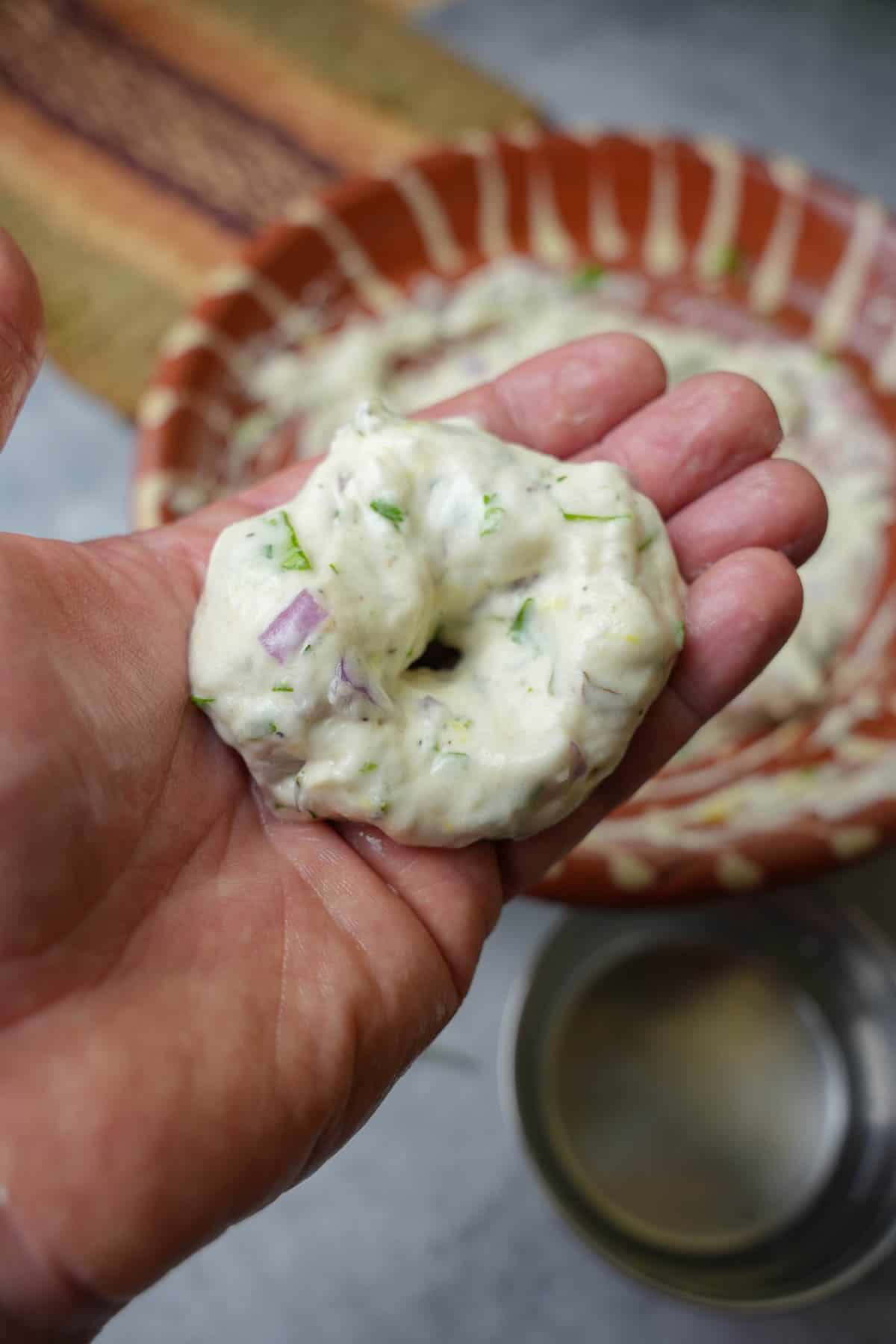 A small portion of the batter is formed into a donut shape. it is show being held in the hand over the bowl of batter.
