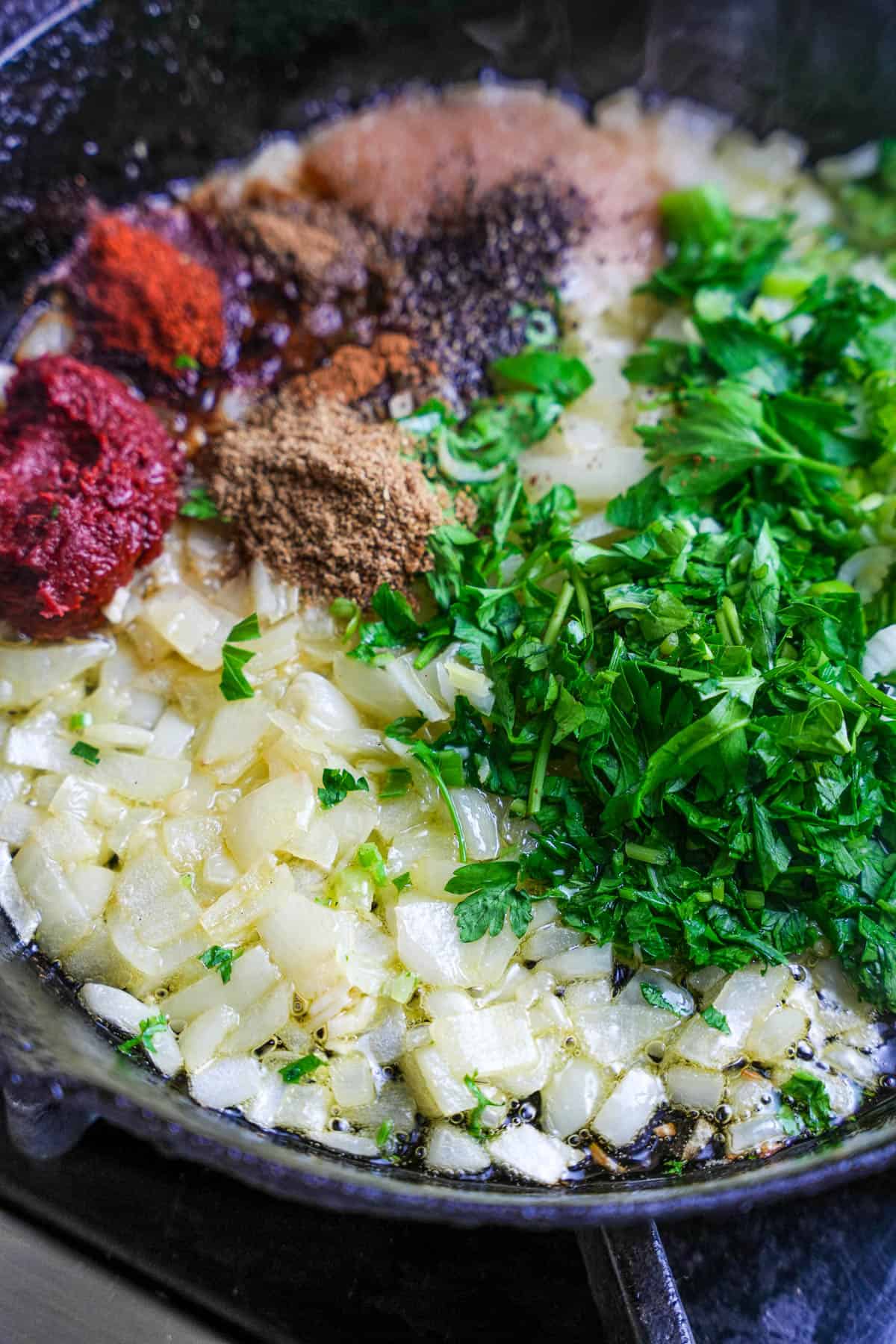 Pepper paste, parsley, and spices are added to the lightly golden, softened onions and garlic in a cast iron skillet.