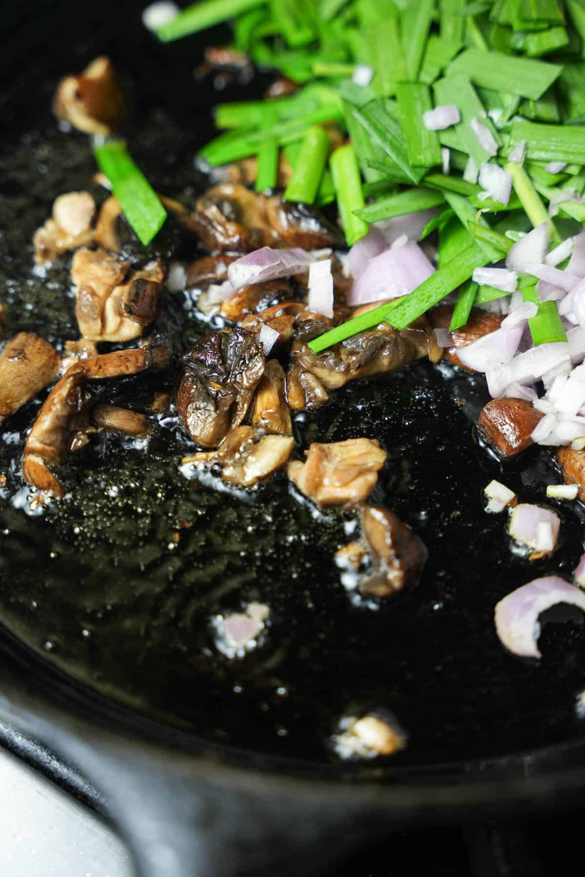 Shallots and chives are added to the cooking mushrooms.