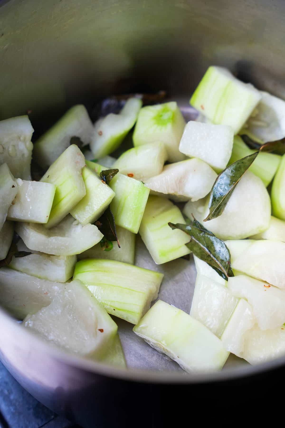 Peeled gourd is sautéed with chilies and curry leaves in a stainless steel pot.