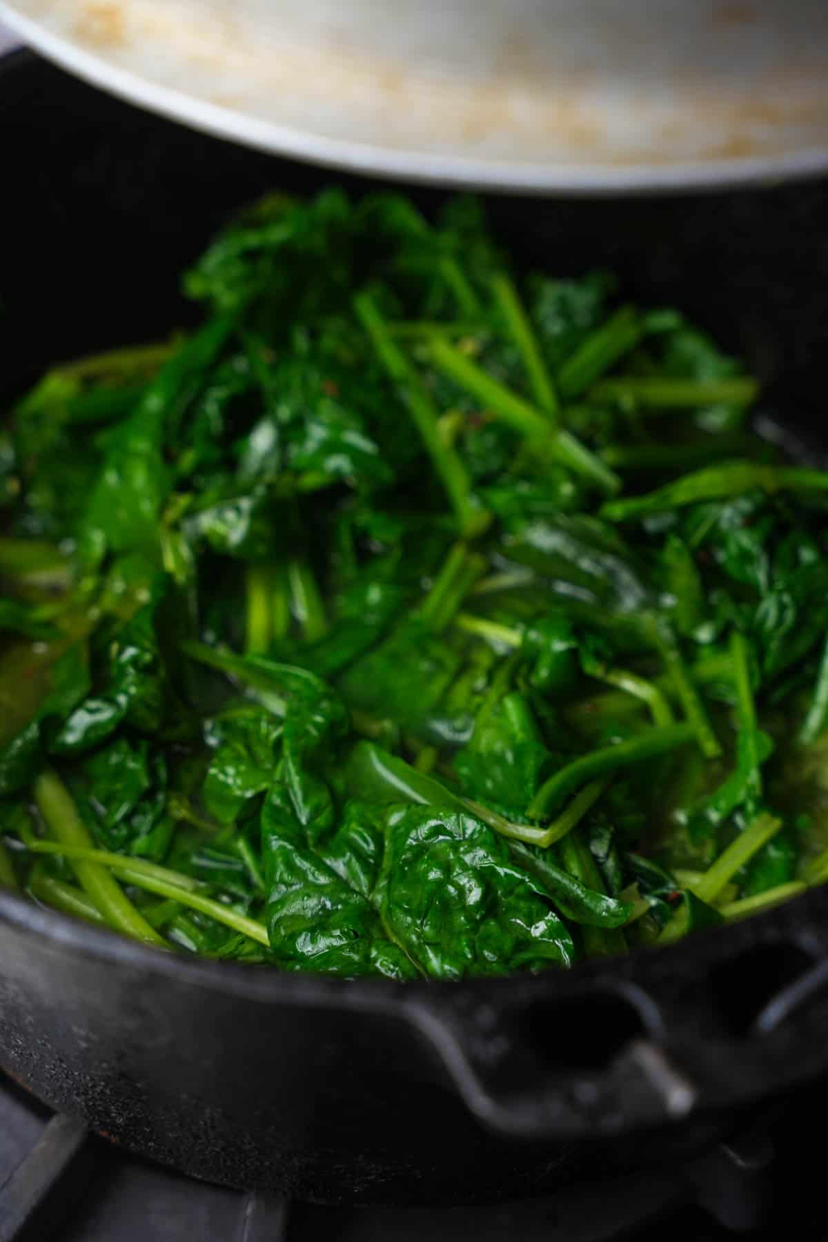 A lid is placed onto the cooking spinach so that it can steam as it cooks.