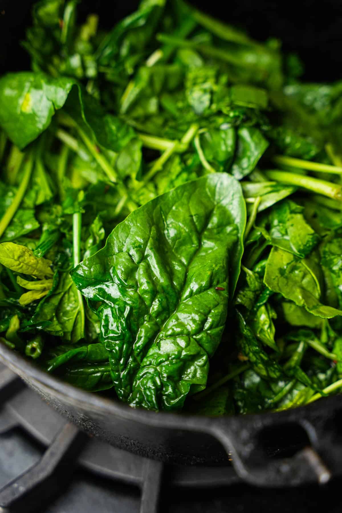 Mature spinach is cooking in a dark colored pan.