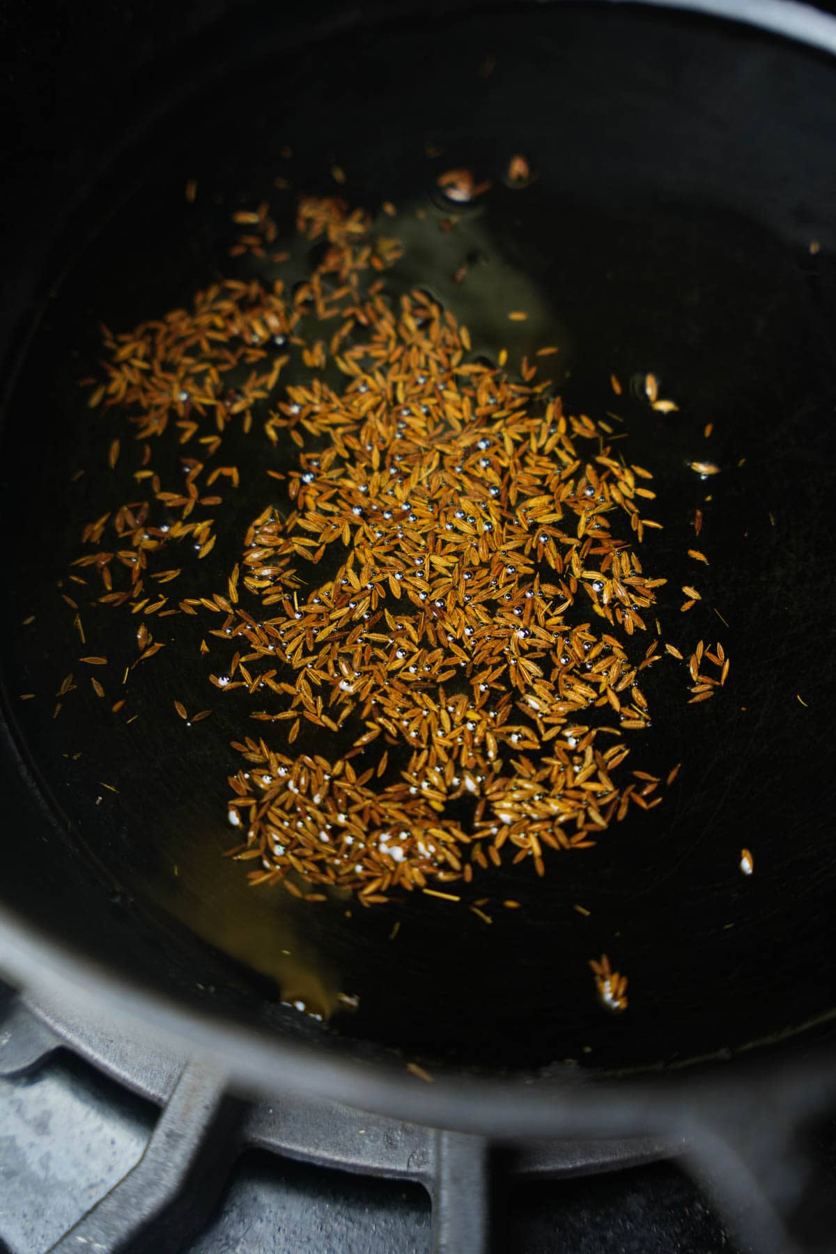 Cumin seeds being fried in hot oil in a black pan.