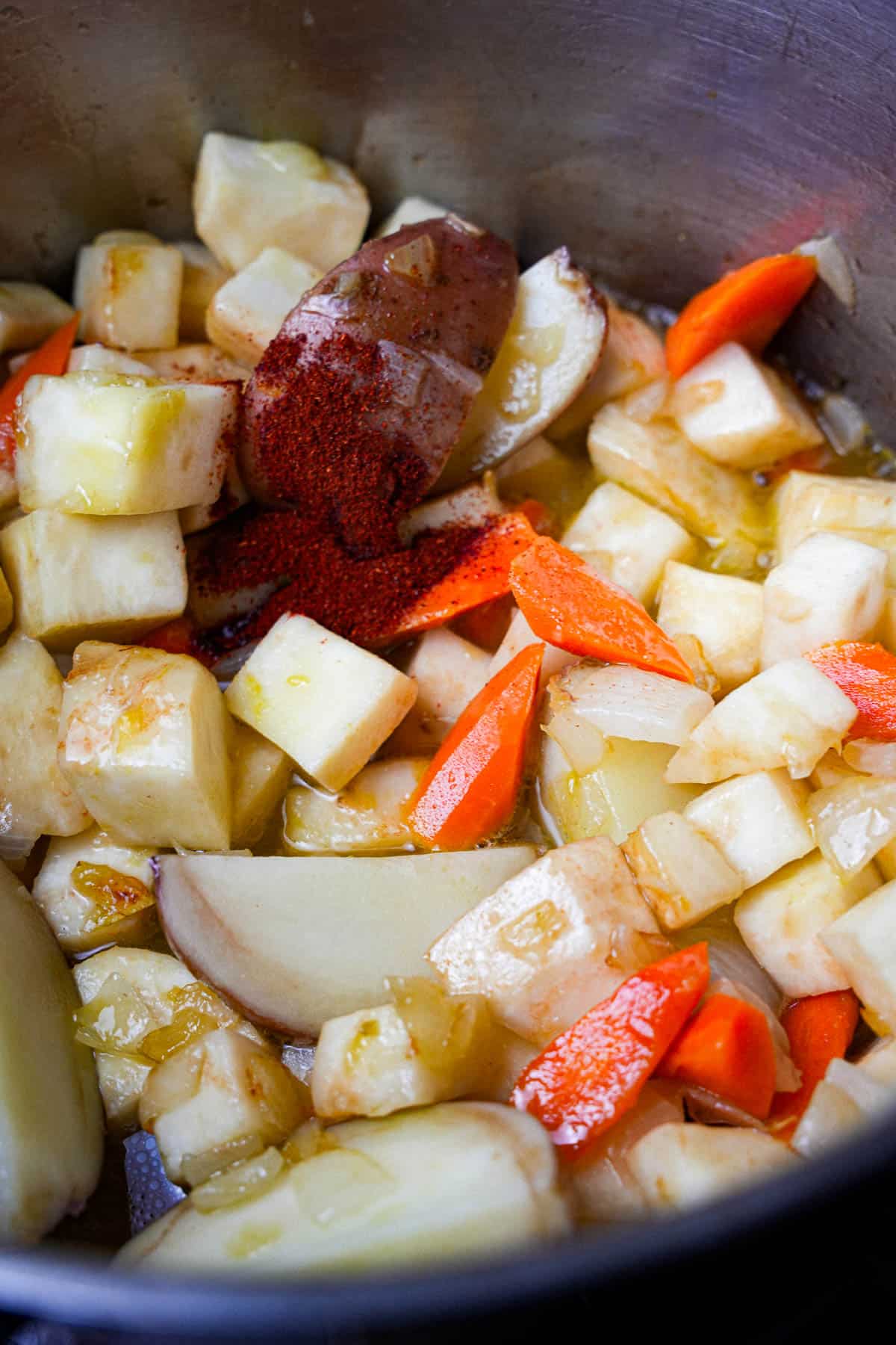 Liquid ingredients and paprika are added to the cooking vegetables in a stainless steel pot.