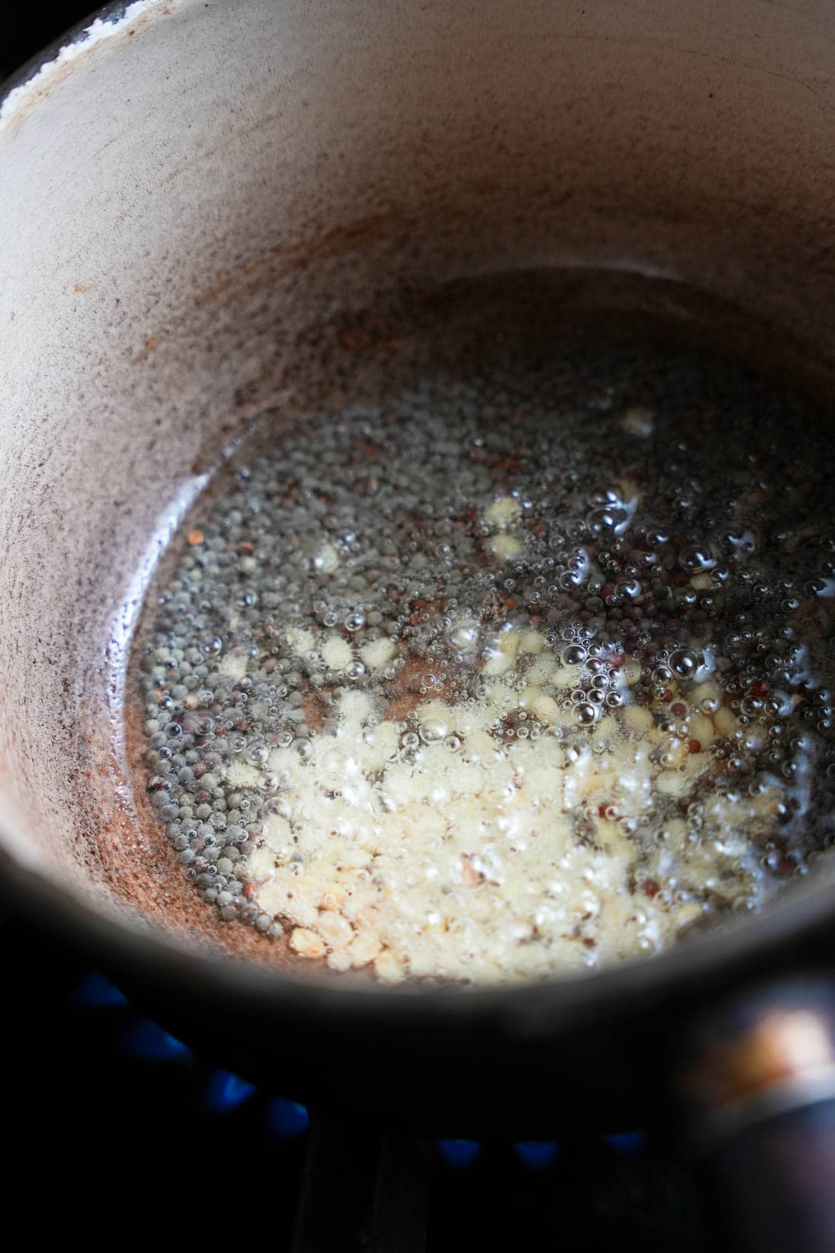Urad dal and mustard seeds are fried in oil in a small pot for making the tadka.