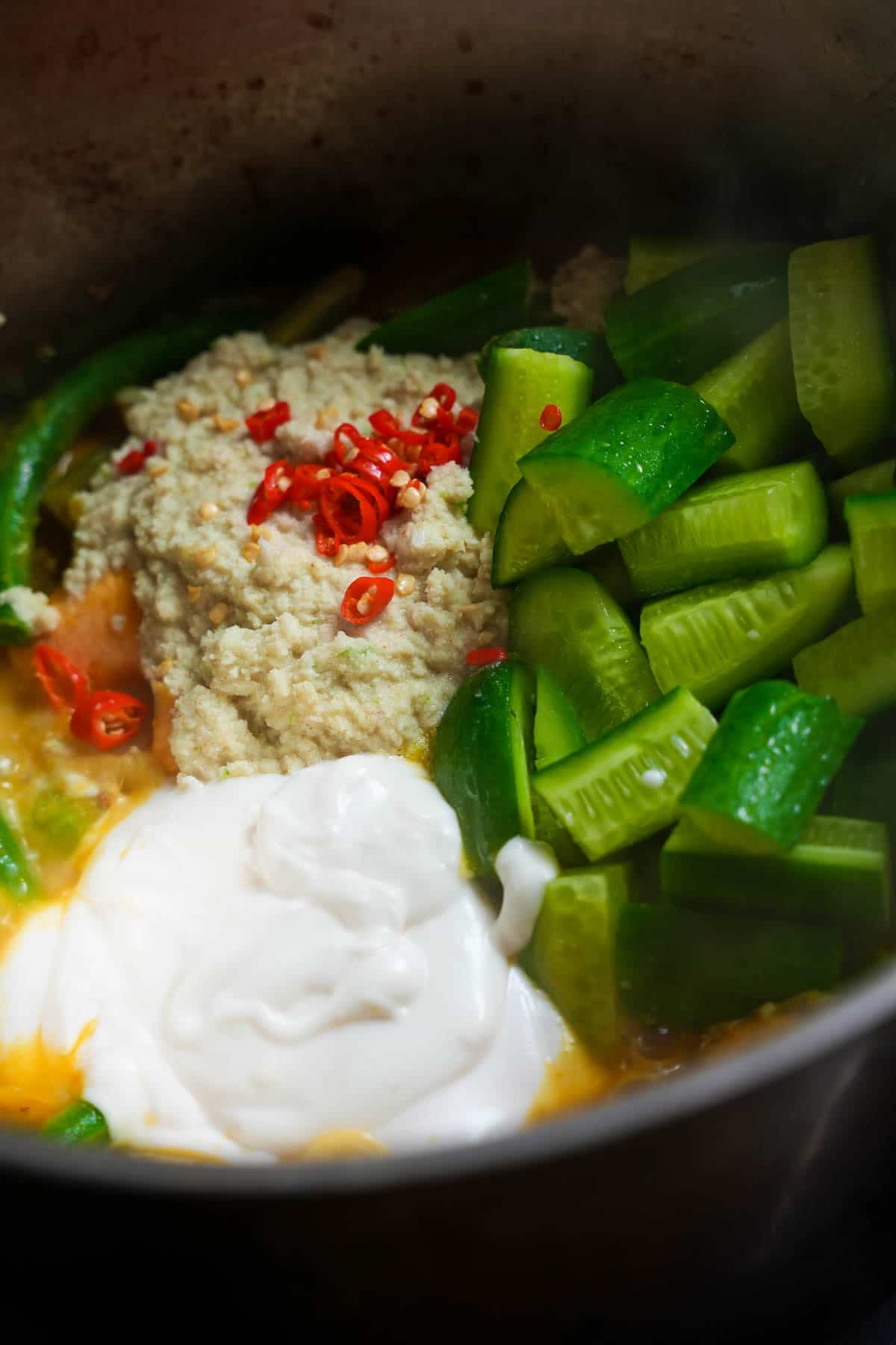 CHilies, the ground coconut mixture, yogurt, and cucumbers are added to the pot.