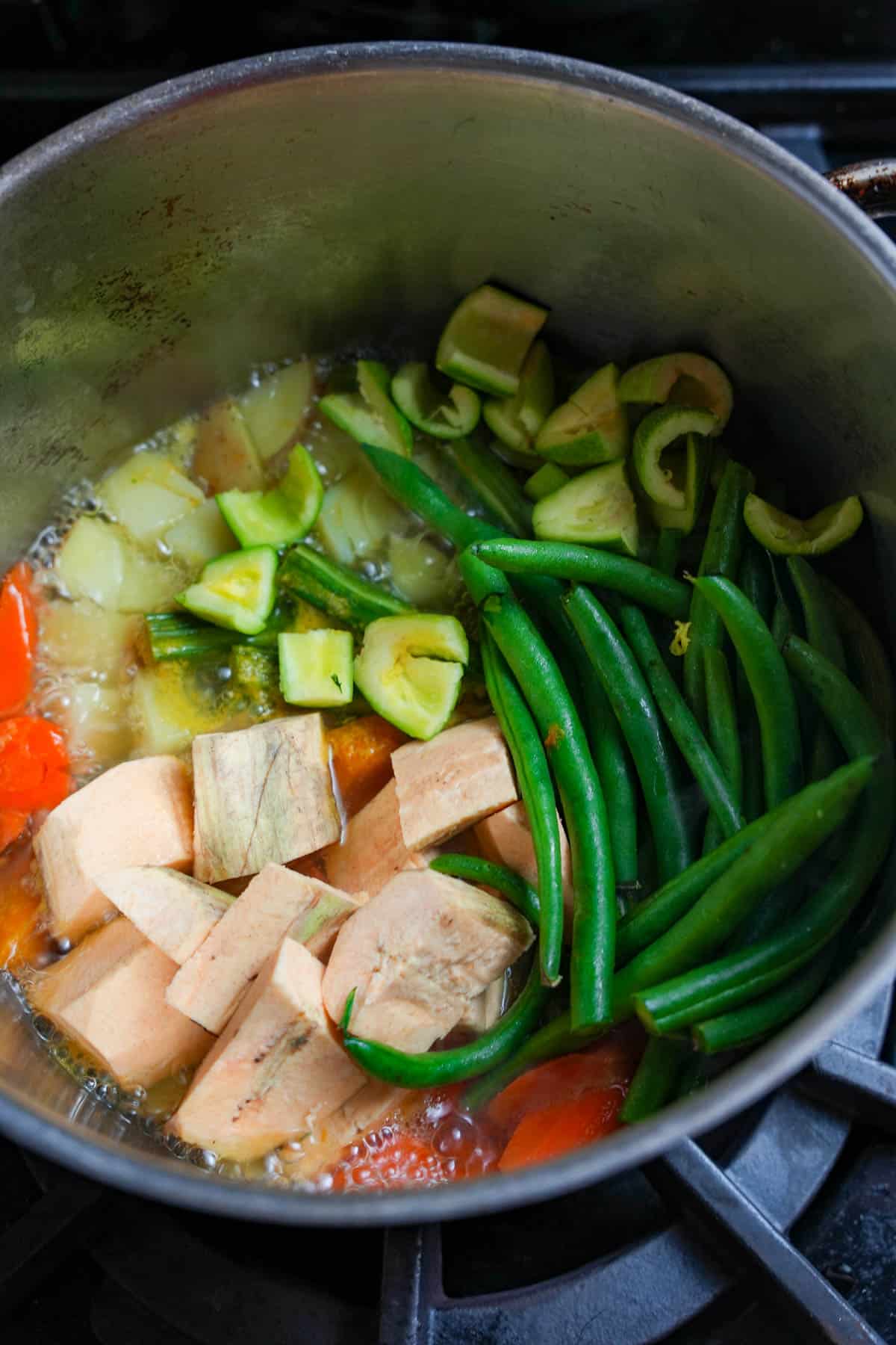 Tindora, string beans and plantain are added to the pot of cooking vegetables on the stove.