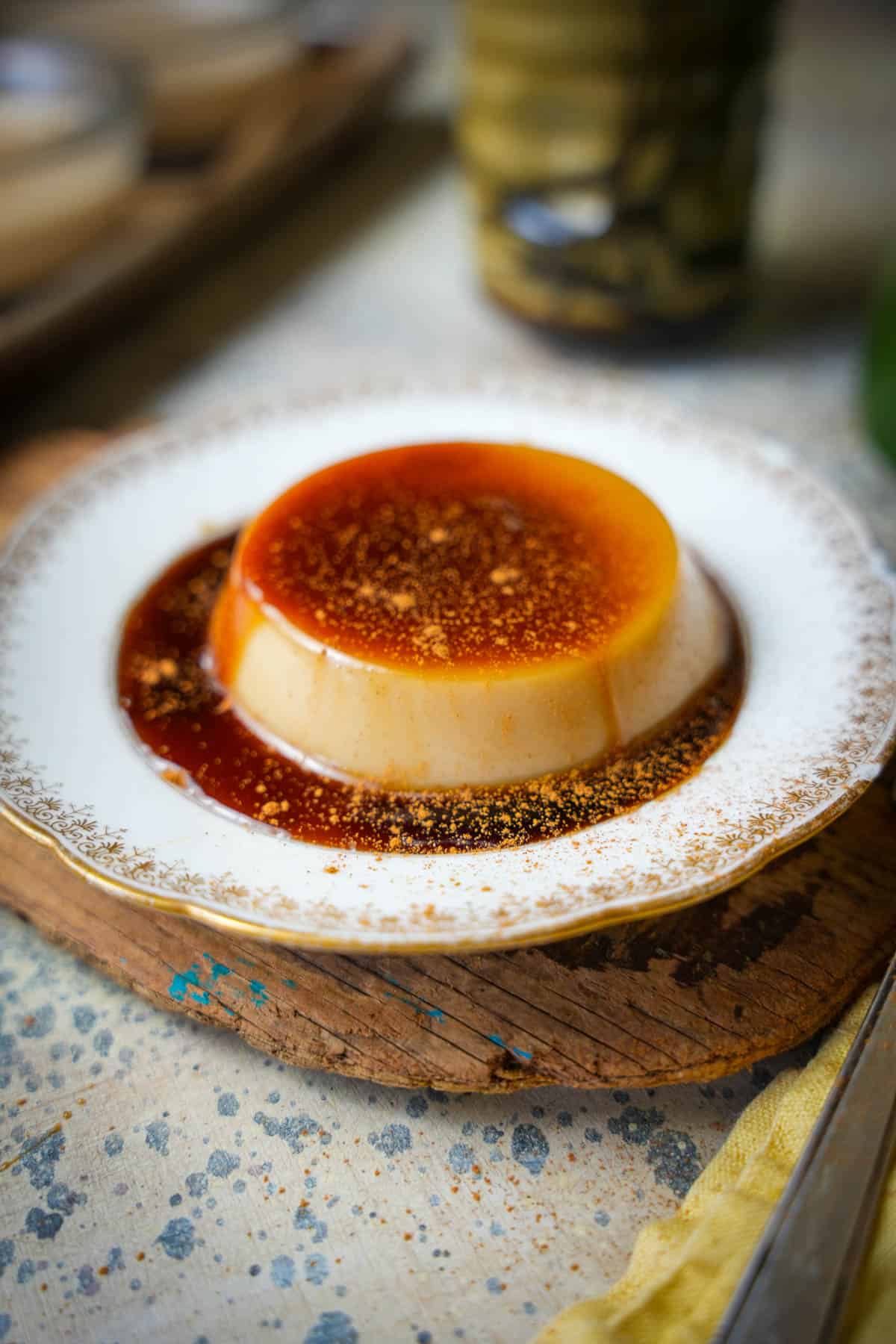 Banh flan on a fancy small plate on top of a wooden surface. Tea, and additional banh fan servings can be seen in the background.