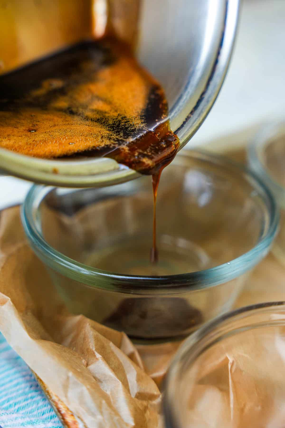 Caramel syrup is poured into glass ramekins on a parchment paper lined baking tray.