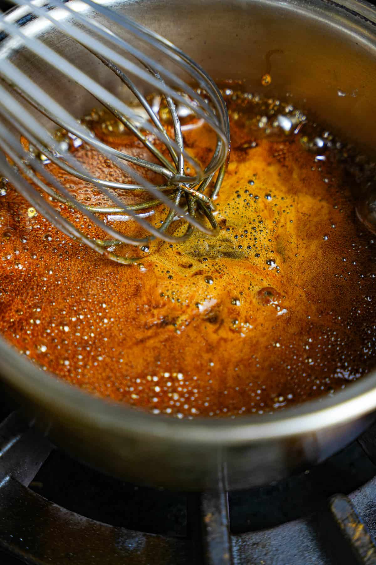 The caramel is whisked as it bubbles in a saucepan.