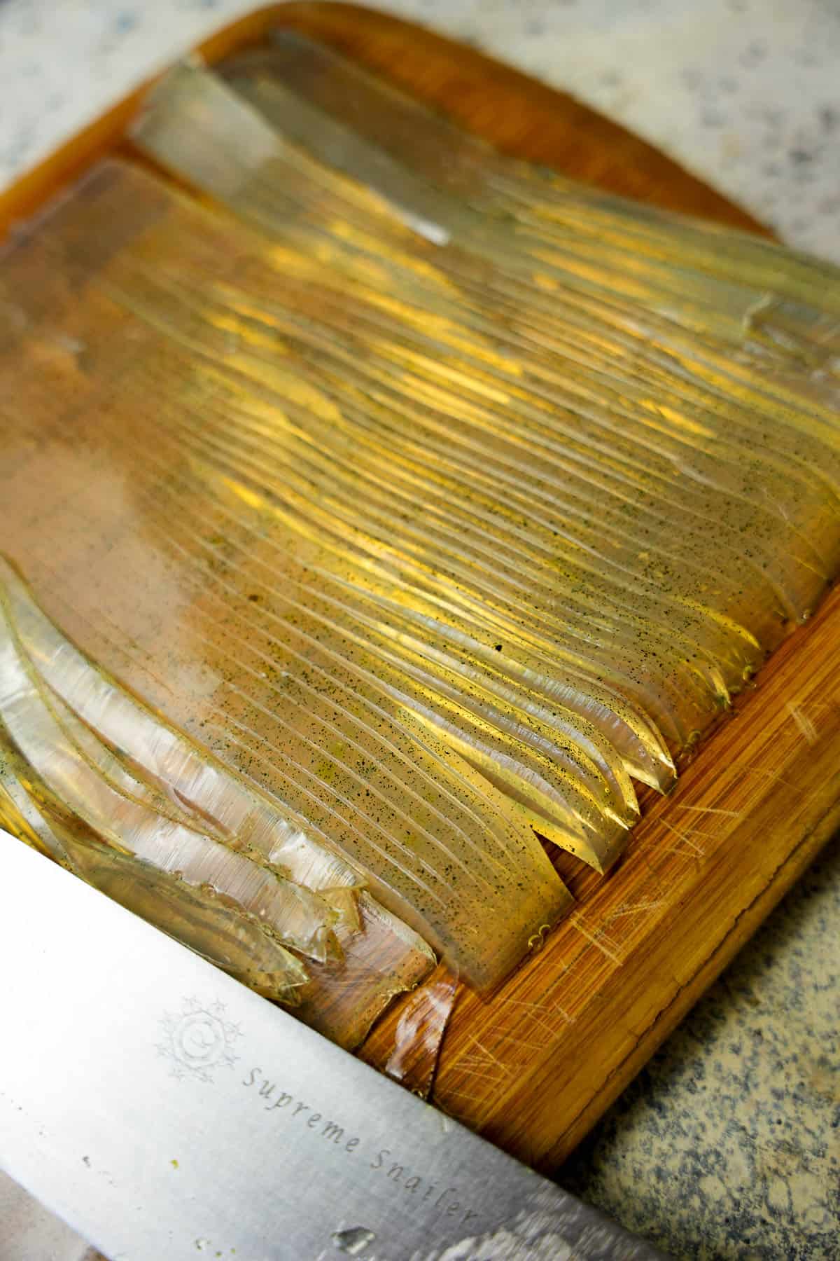 the pandan jelly is thinly sliced into semi-transparant noodles with a sharp knife on a cutting board.