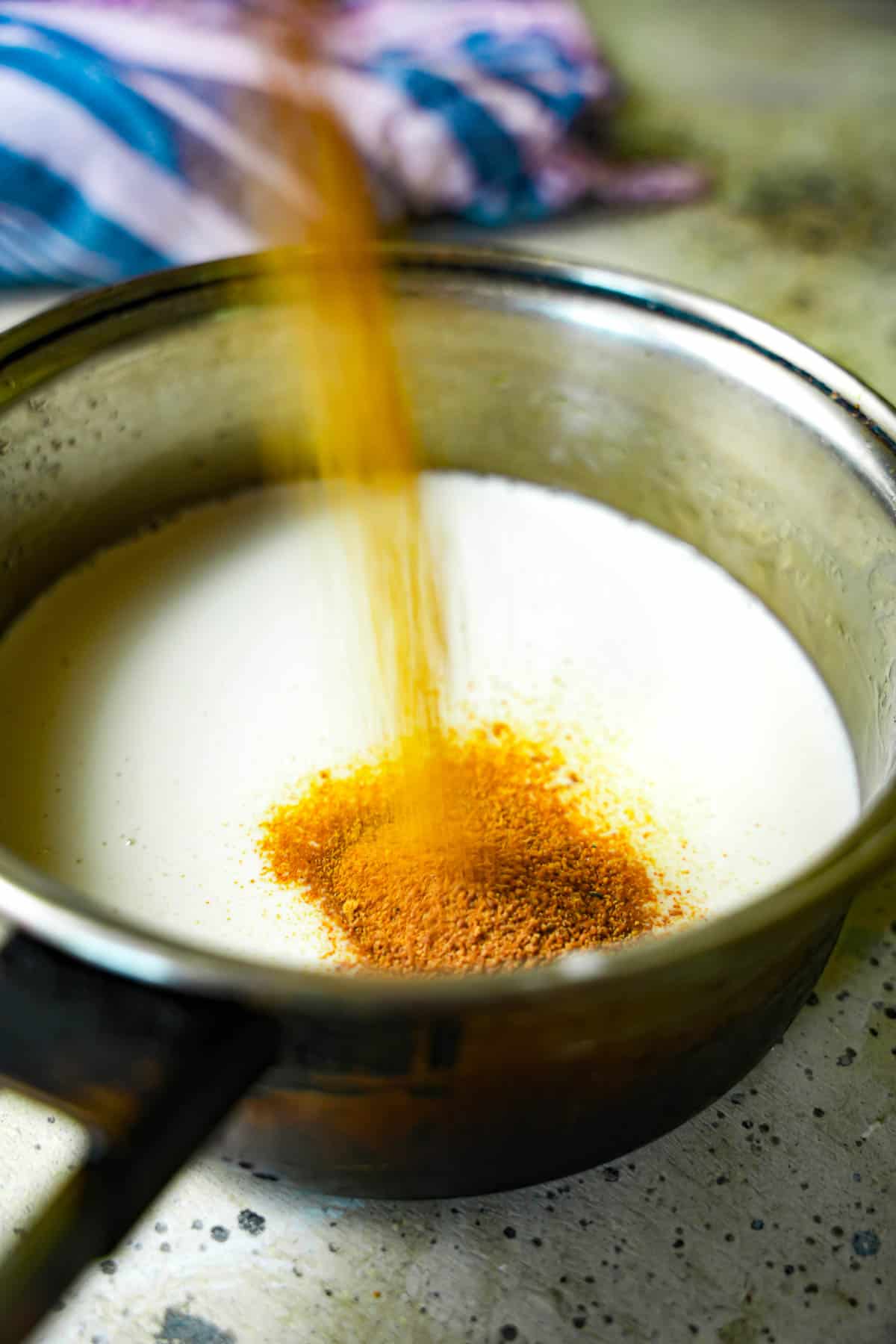 Coconut cream in a saucepan with coconut sugar being poured into it.