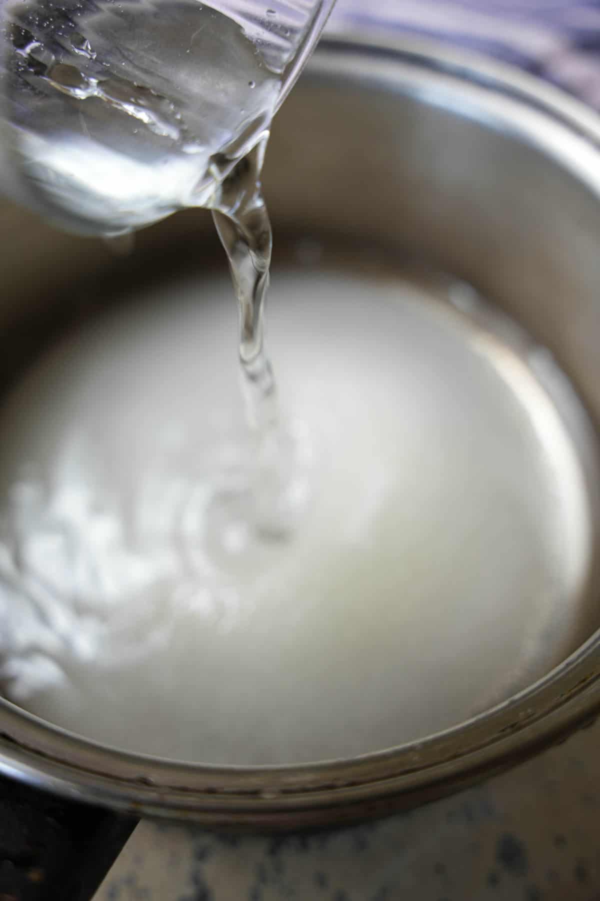 Water and sugar are mixed together to make the sugar syrup in a saucepan.